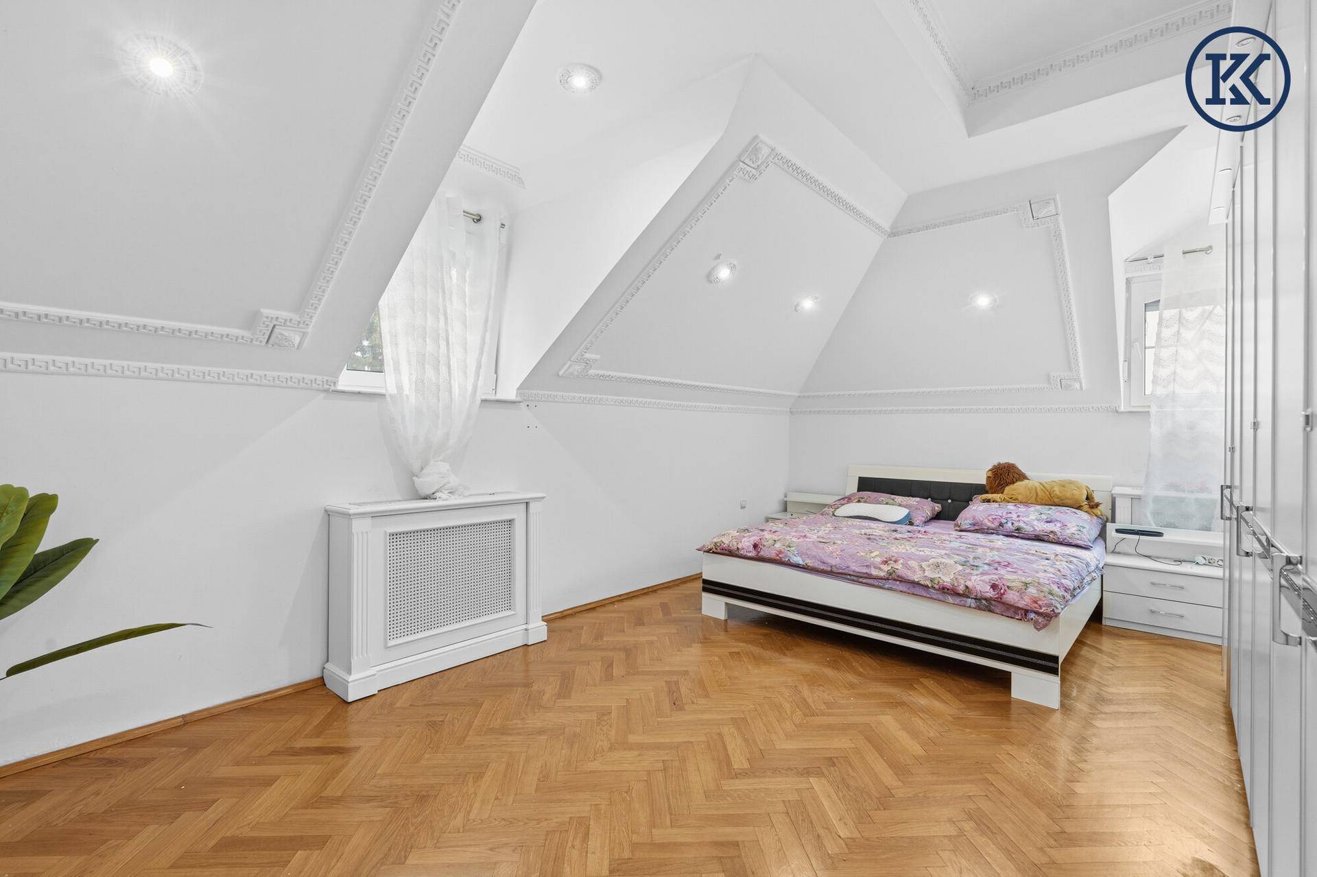 Gemütliches Schlafzimmer im Dachgeschoss mit Holzboden, Dachschrägen und dekorativen Deckenleisten.