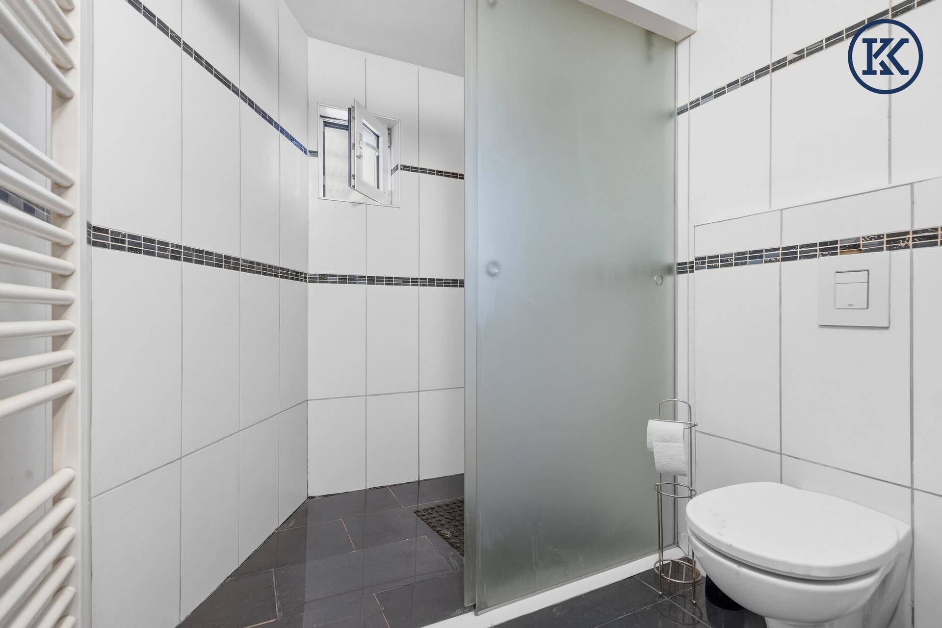 Modernes Badezimmer mit Duschkabine, weißen Fliesen und beheiztem Handtuchhalter.