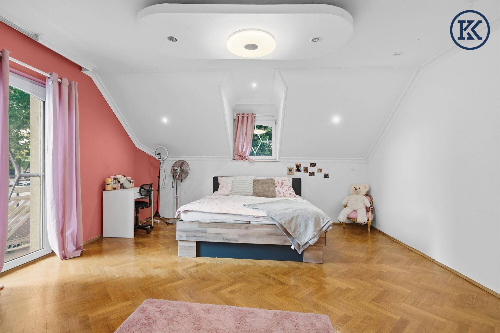 Schlafzimmer mit Holzboden, rosa Akzentwand und Fenster mit Blick ins Grüne.