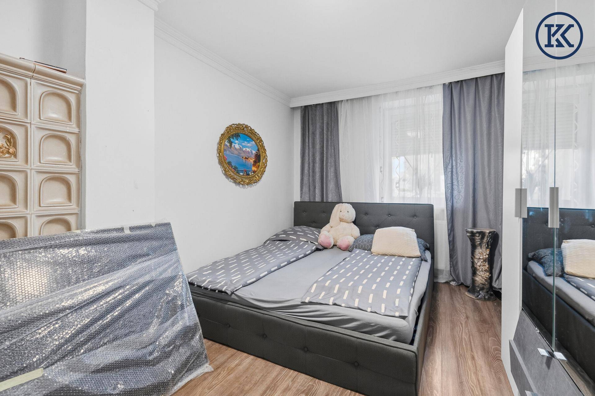 Schlafzimmer mit Holzboden, Kachelofen und großem Fenster.