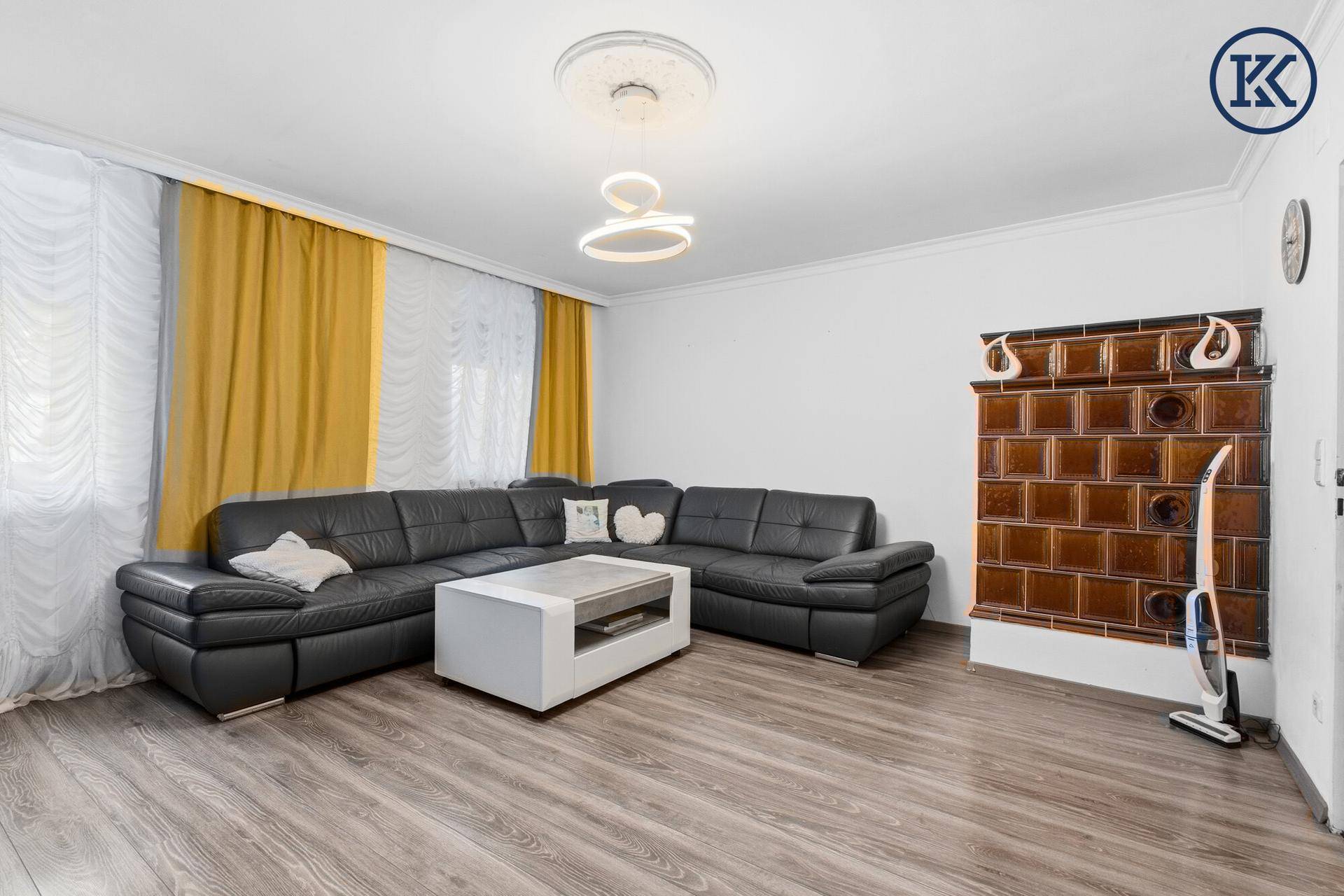Gemütliches Wohnzimmer mit Ledersofa, Holzboden und traditionellem Kachelofen.