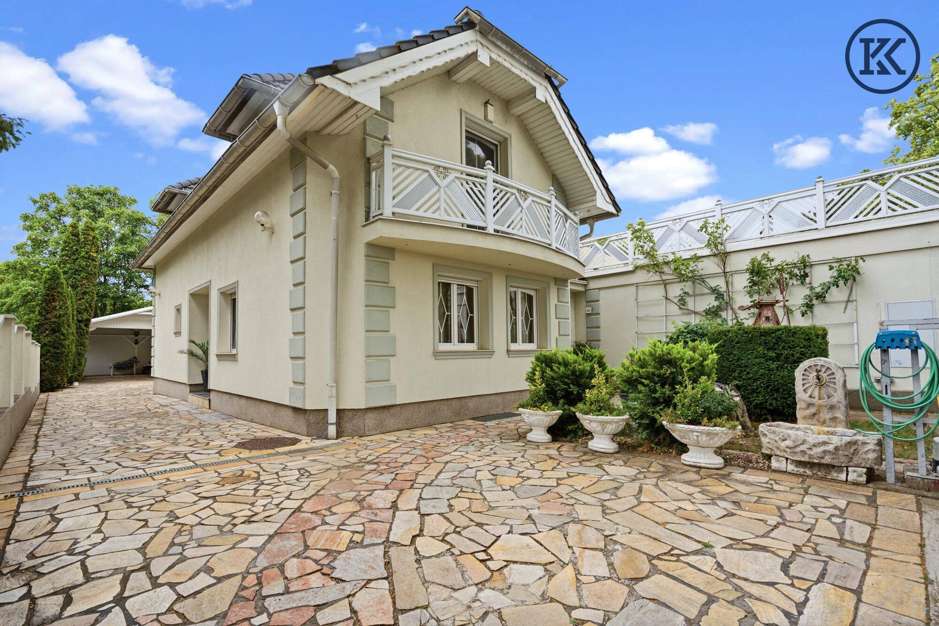 Vorderansicht des Hauses mit Balkon, Naturstein-Zufahrt und dekorativen Pflanzgefäßen.