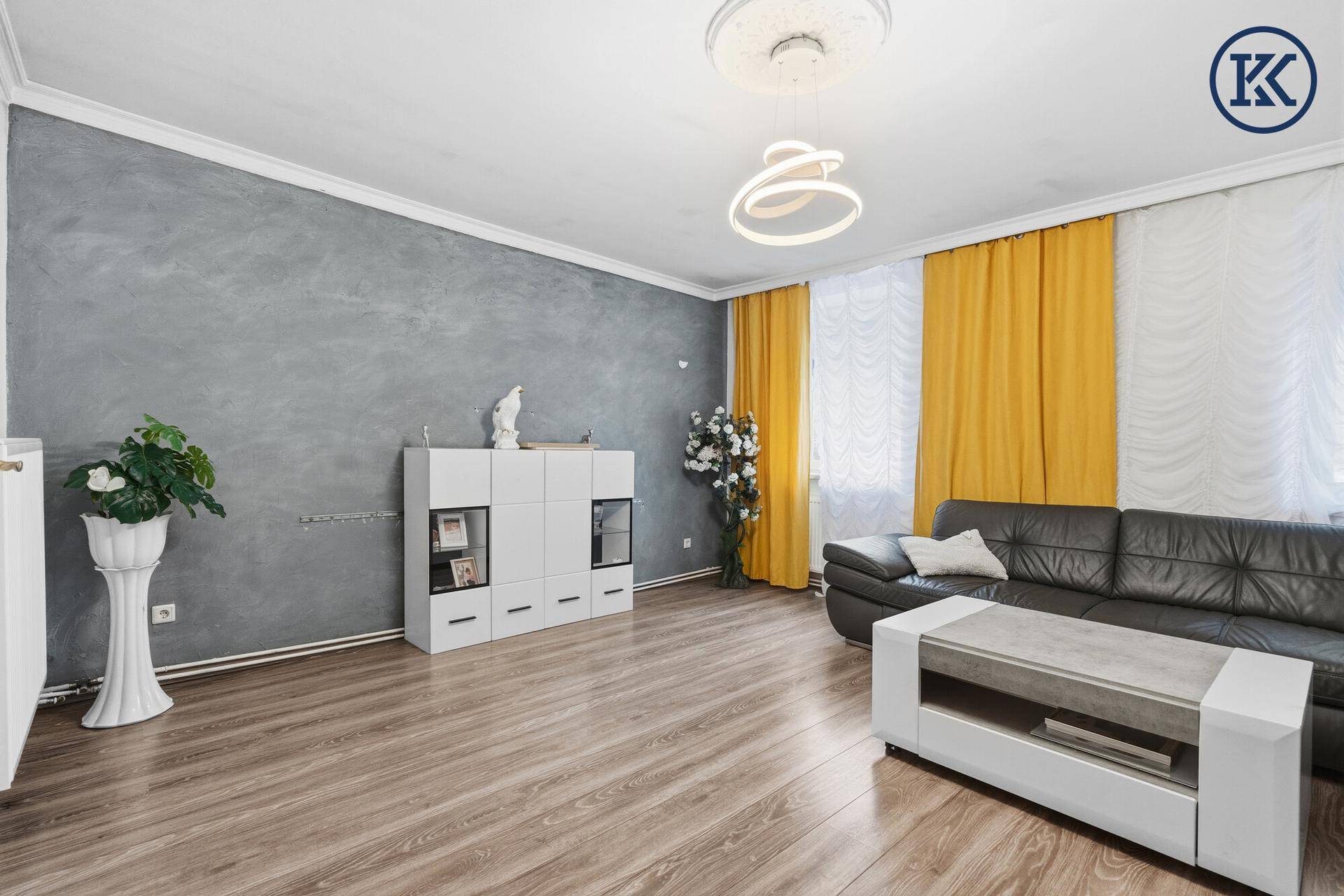 Wohnzimmer mit grauer Akzentwand, Ledersofa und Laminatboden.