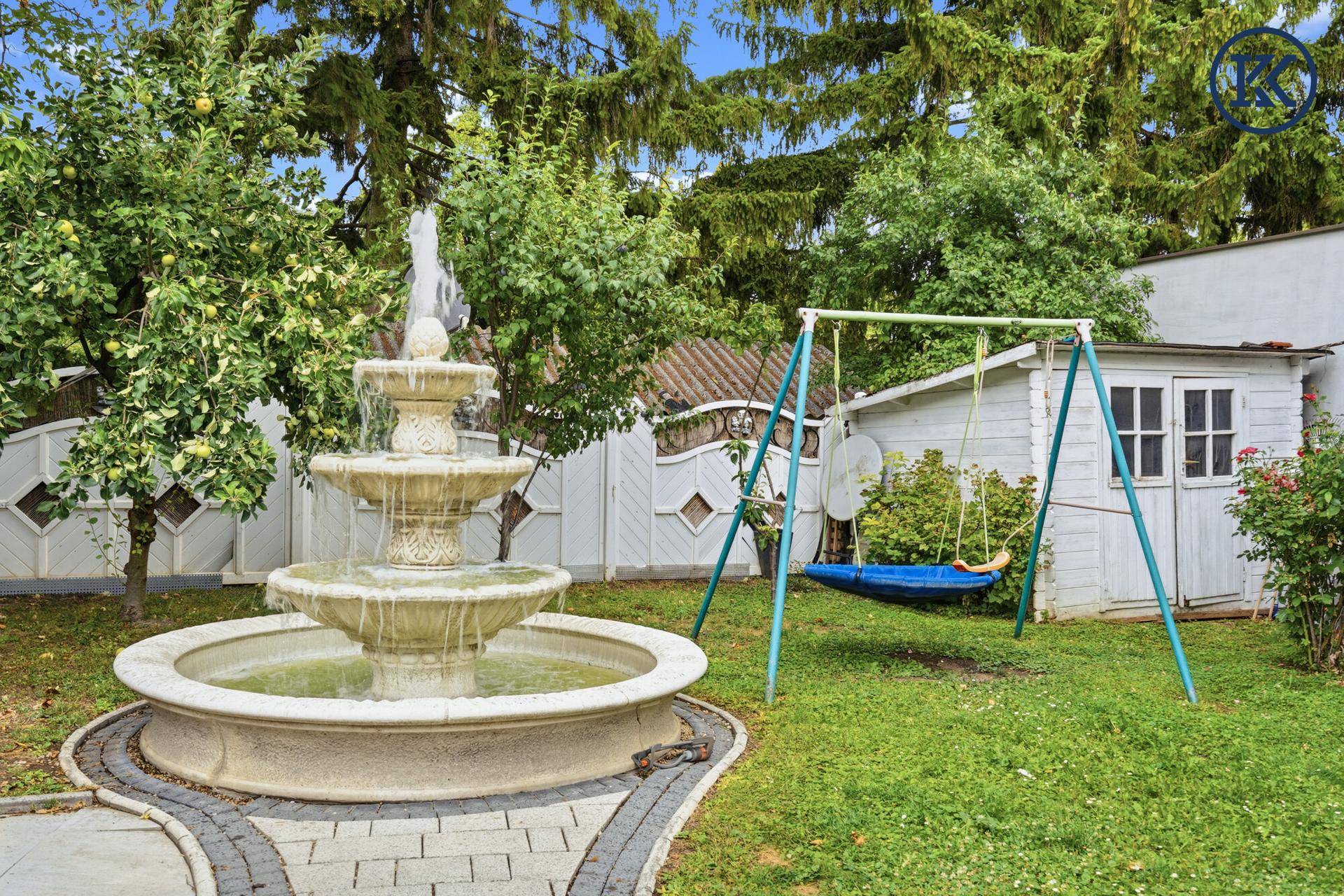 Grüner Garten mit Springbrunnen, Schaukel und einem kleinen Gartenhaus.