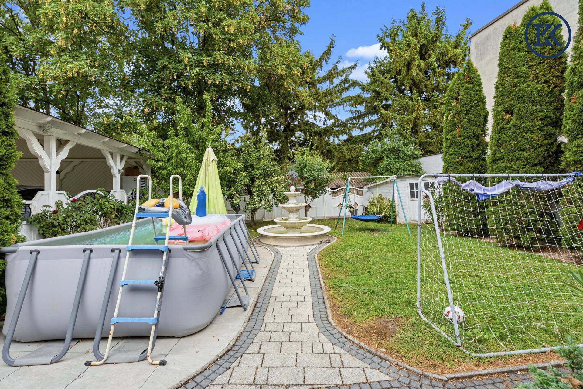 Geräumiger Garten mit Aufstellpool, gepflastertem Weg und Fußballtor.