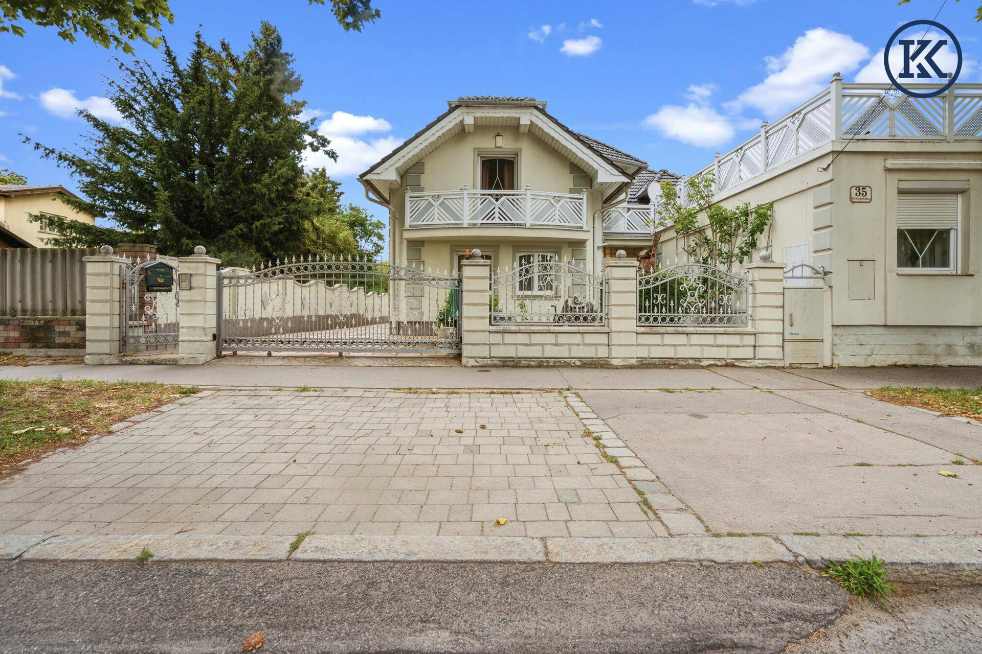 Ansicht des Hauses von der Straße mit Zaun und gepflastertem Vorplatz.