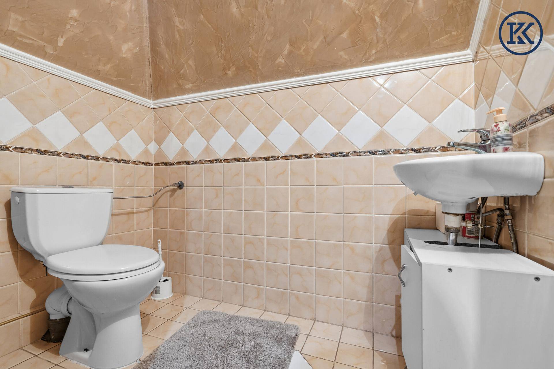 Kleines Gäste-WC mit WC, Waschbecken und beigefarbenen Fliesen.