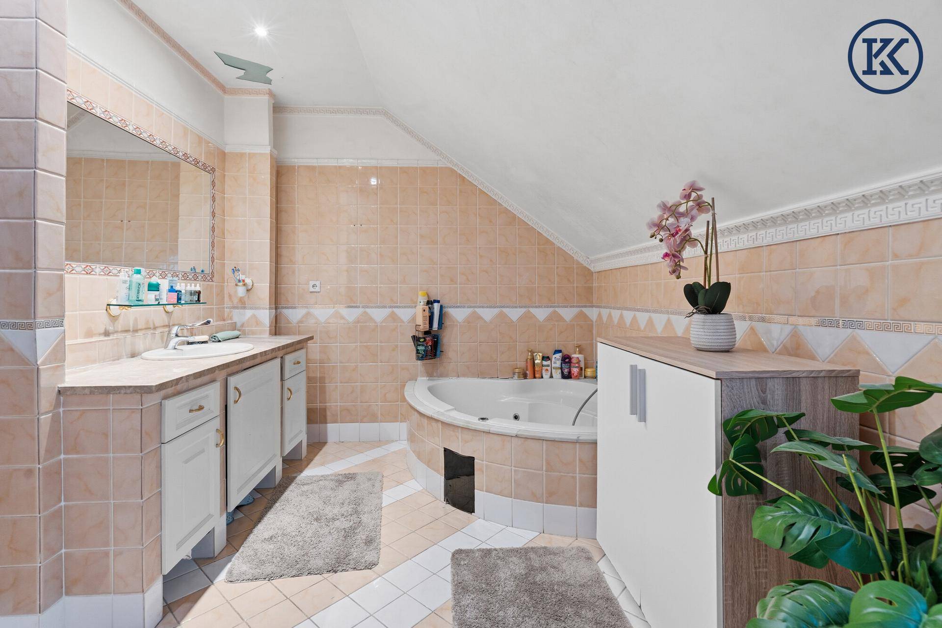 Geräumiges Badezimmer im Dachgeschoss mit Eckbadewanne, Doppelwaschbecken und beigefarbenen Fliesen.