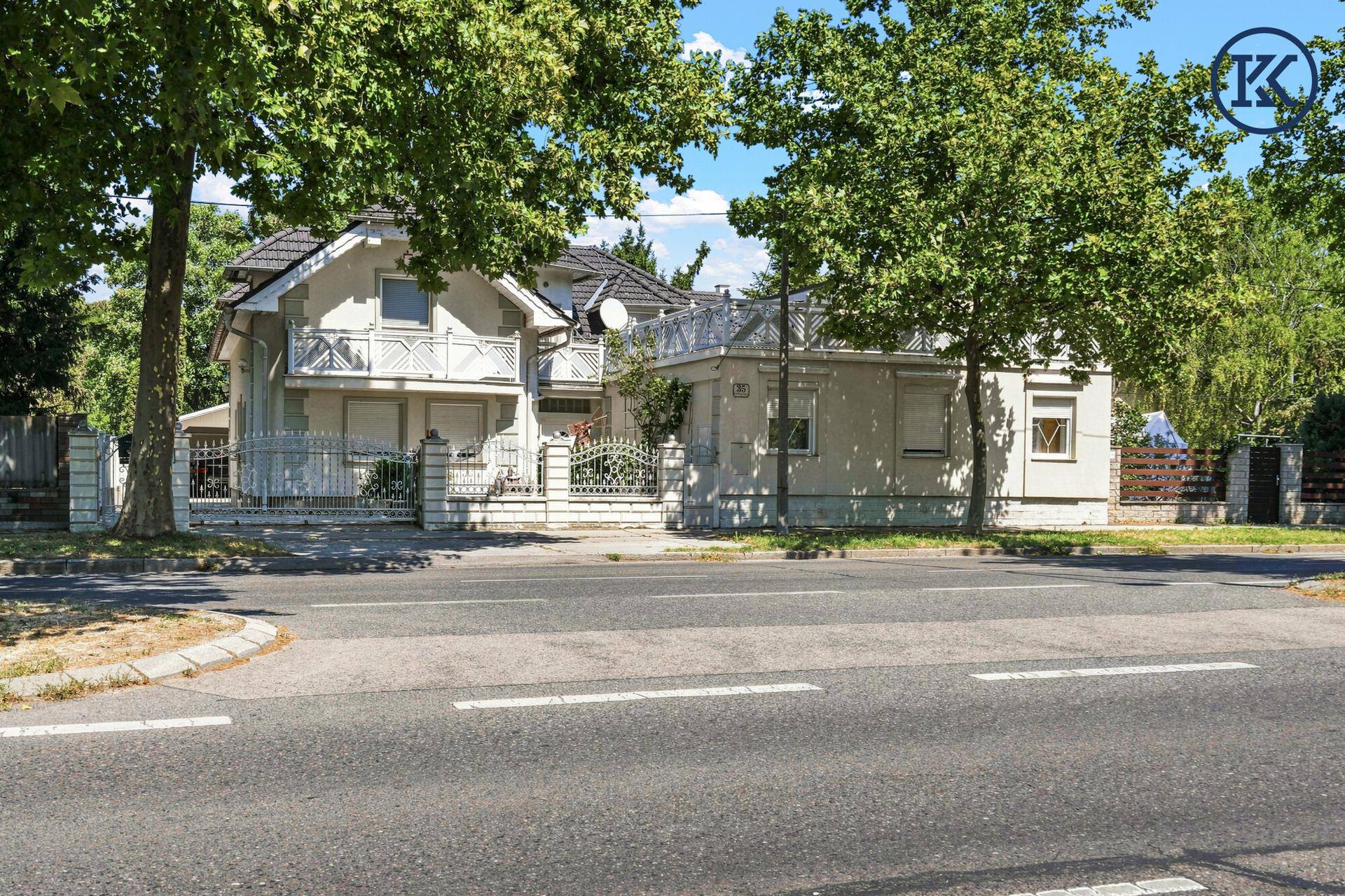 Ansicht des Hauses von der Straße mit gepflegtem Vorgarten und hohen Bäumen.