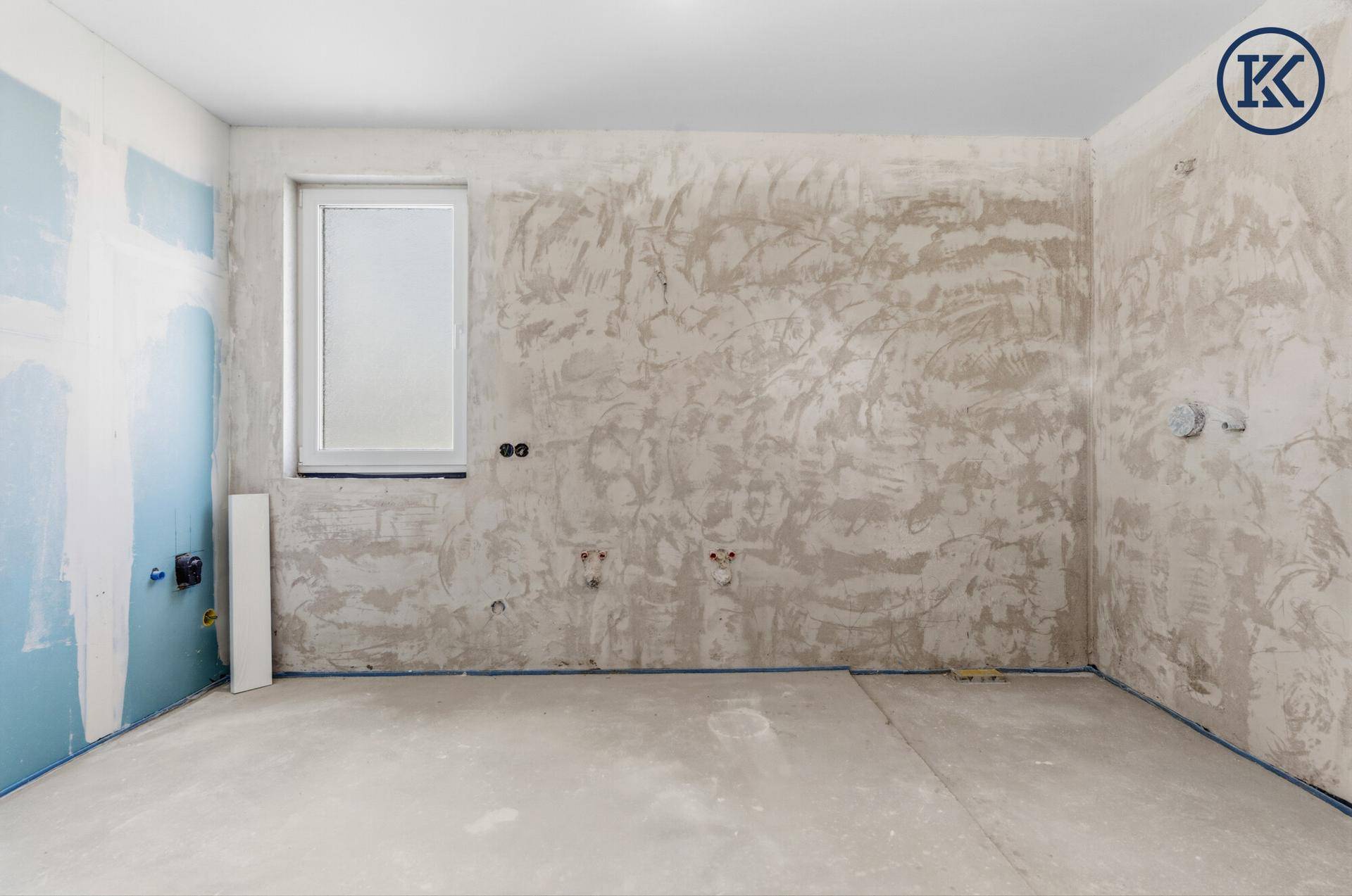 Badezimmer im Rohbau mit vorbereiteten Anschlüssen und einem Fenster, bereit für die Installation.
