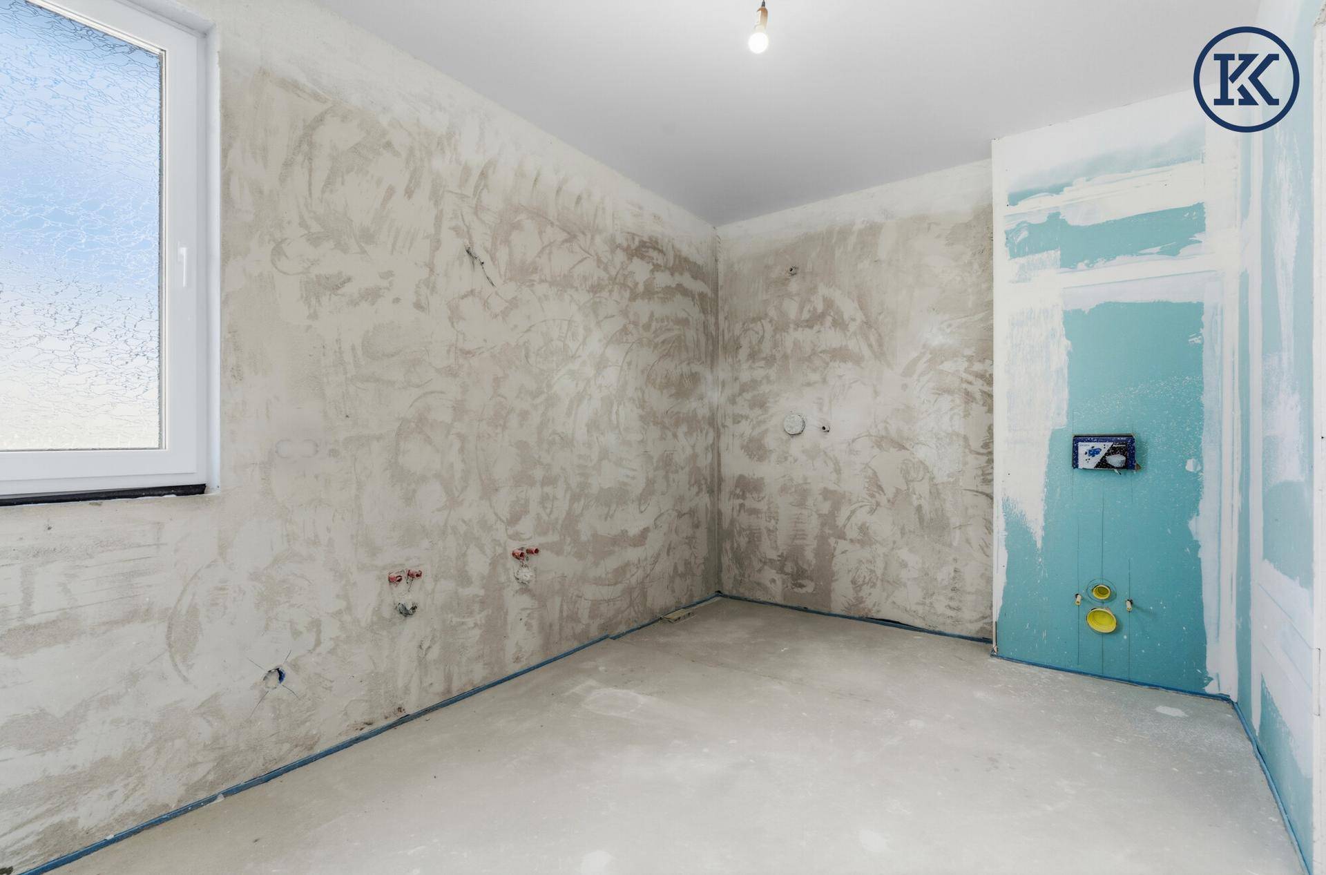 Badezimmer im Rohbau mit Fenster und vorbereiteten Anschlüssen für Badewanne oder Dusche.