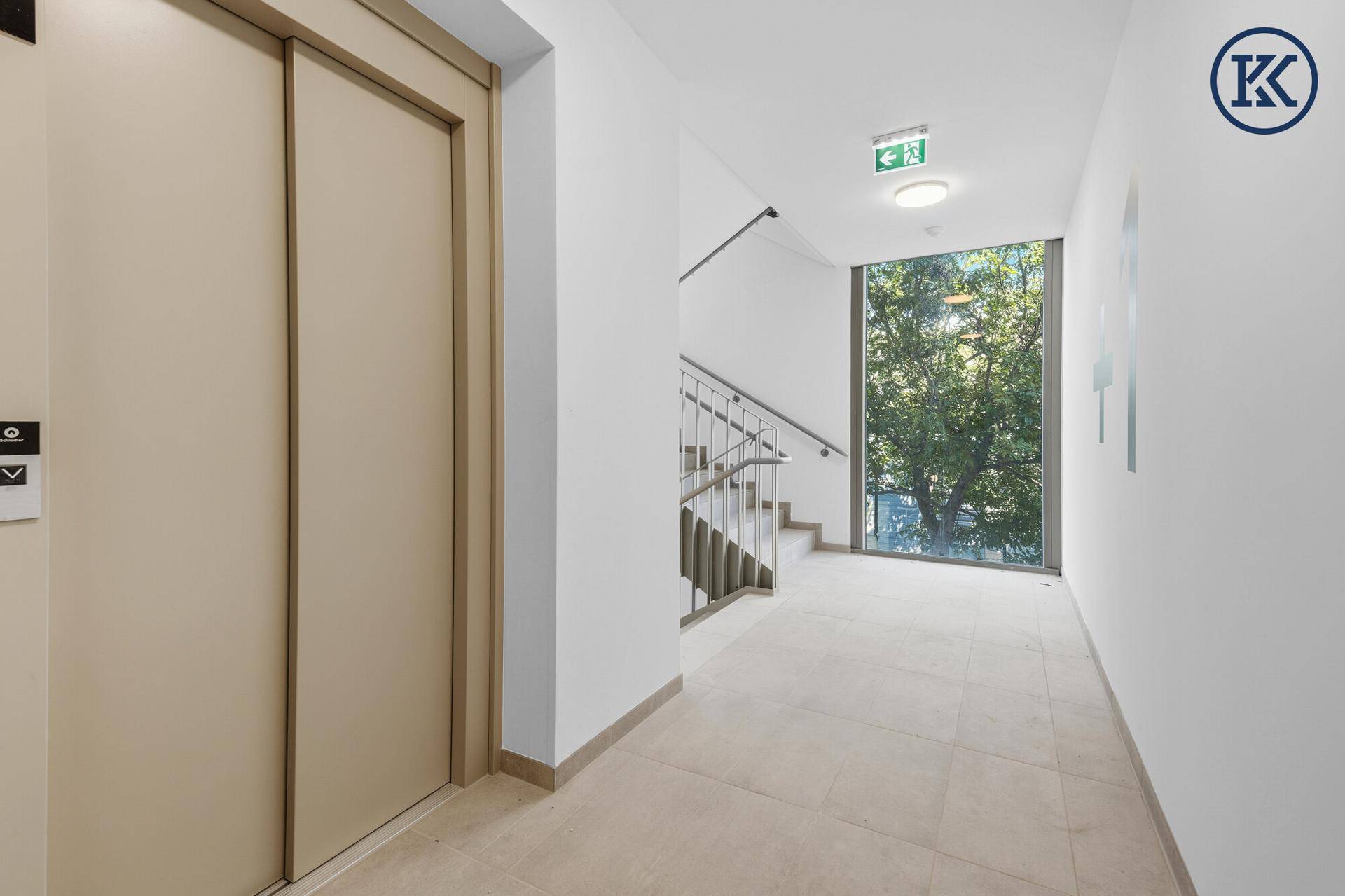 Moderner Flur mit Aufzug und Treppenhaus, das durch ein großes Fenster viel Tageslicht erhält.