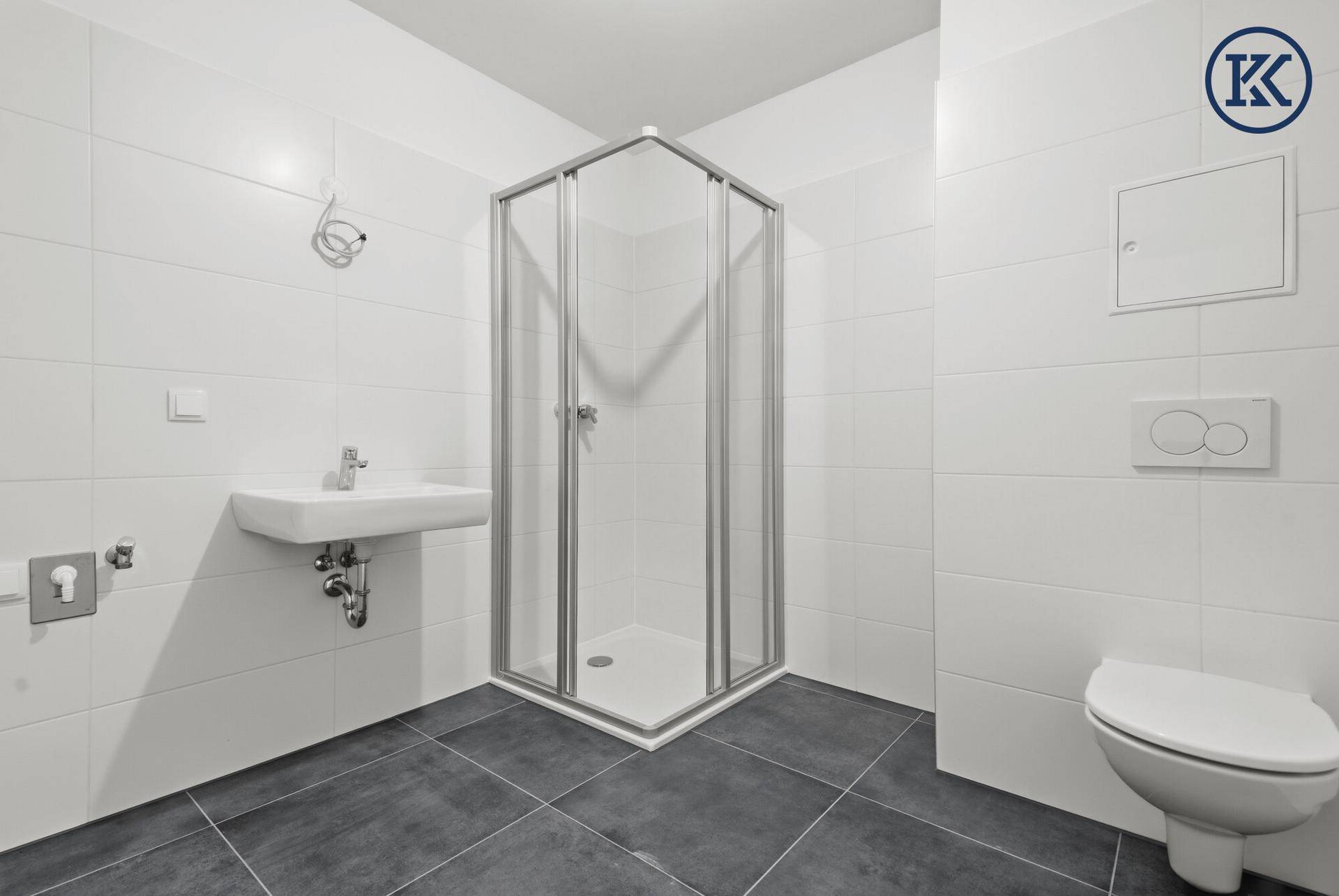 Modernes Badezimmer mit weißen Wandfliesen, dunklem Boden, Eckdusche und wandhängendem WC.