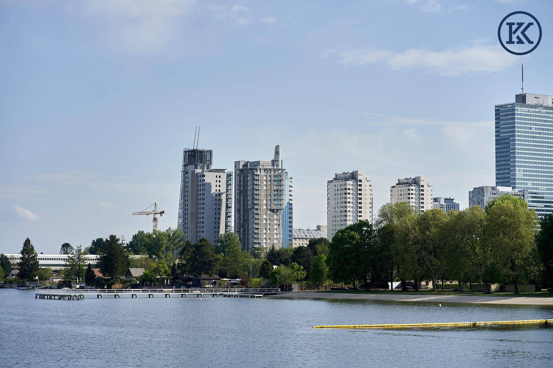 Weitläufiger Blick über den See auf die beeindruckende Skyline mit modernen Gebäuden und viel Grün.