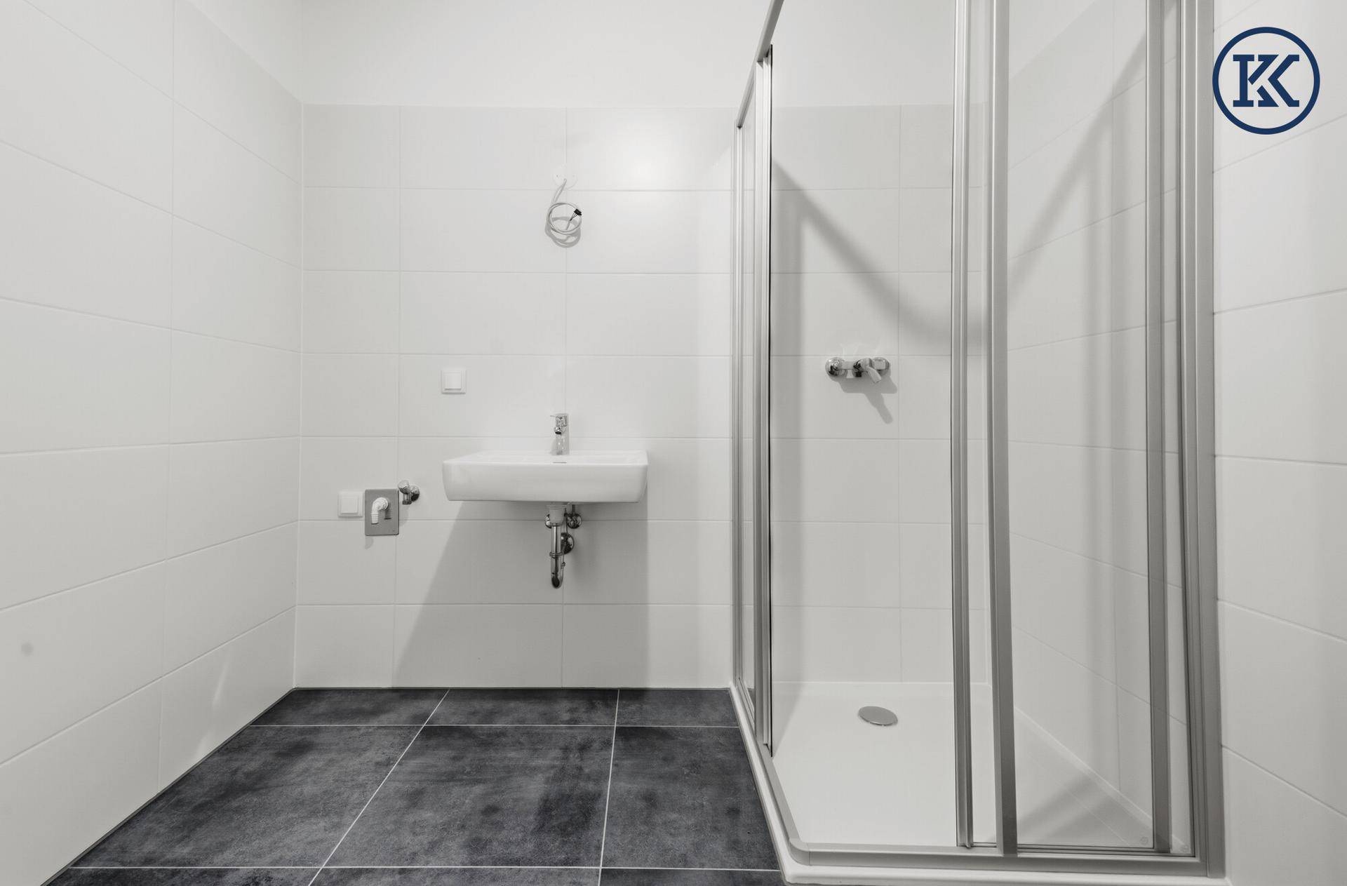 Helles Badezimmer mit Duschkabine, wandhängendem Waschbecken und modernen Fliesen in Weiß und Grau.
