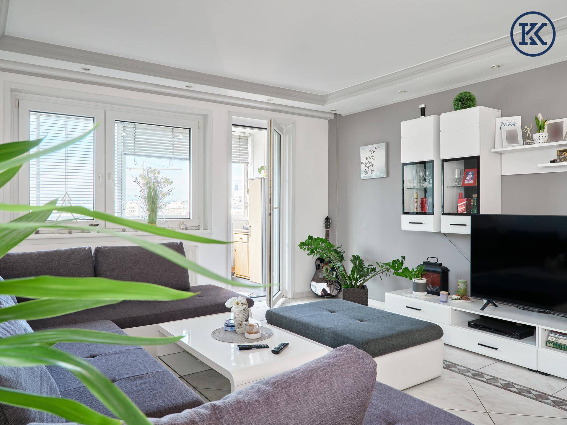Gemütlicher Wohnbereich mit Ecksofa, Couchtisch und Medienwand, hell beleuchtet durch große Fenster.