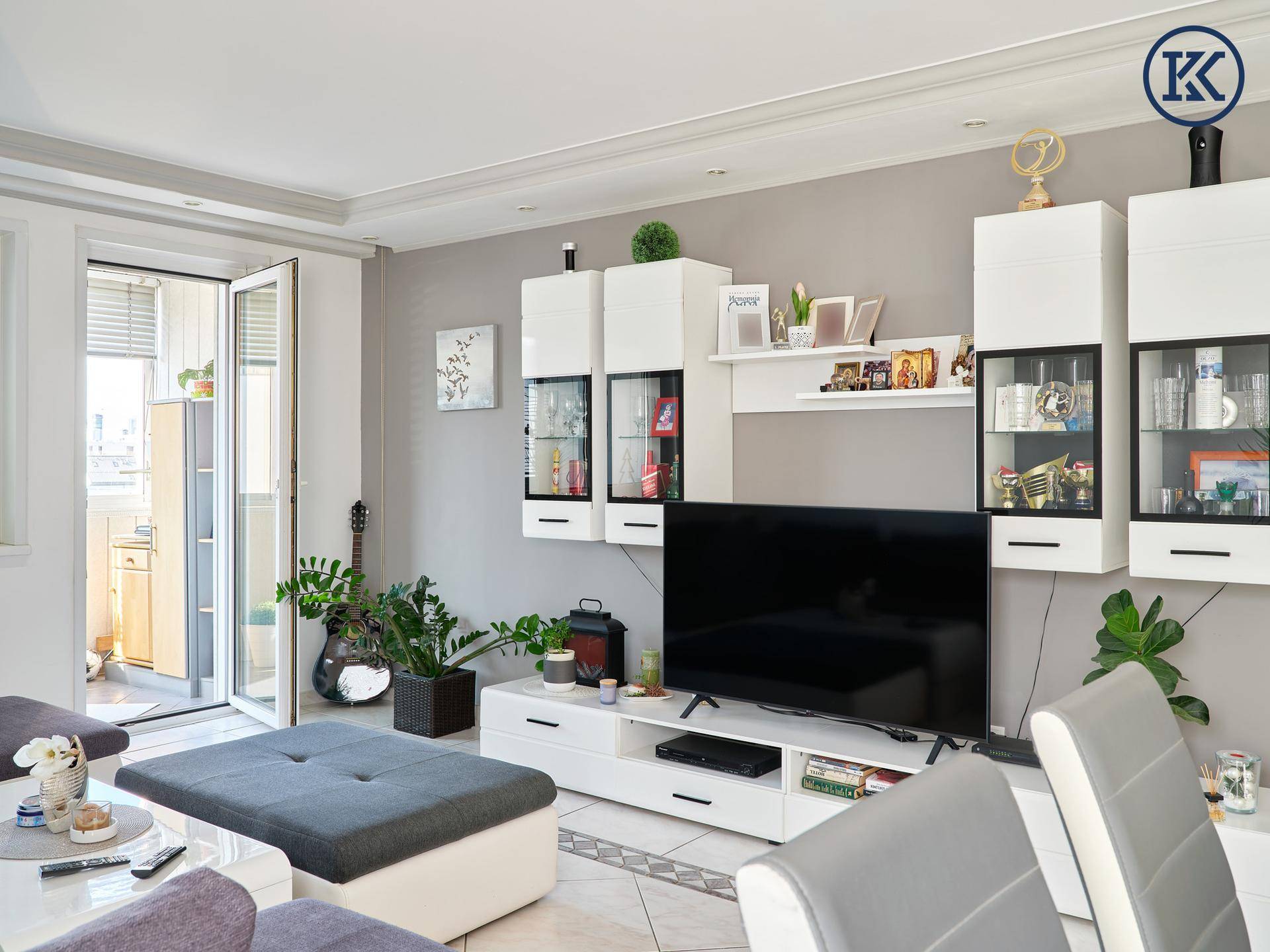Moderner Wohnbereich mit TV-Möbeln, dekorativen Elementen und Zugang zu einem kleinen Balkon.