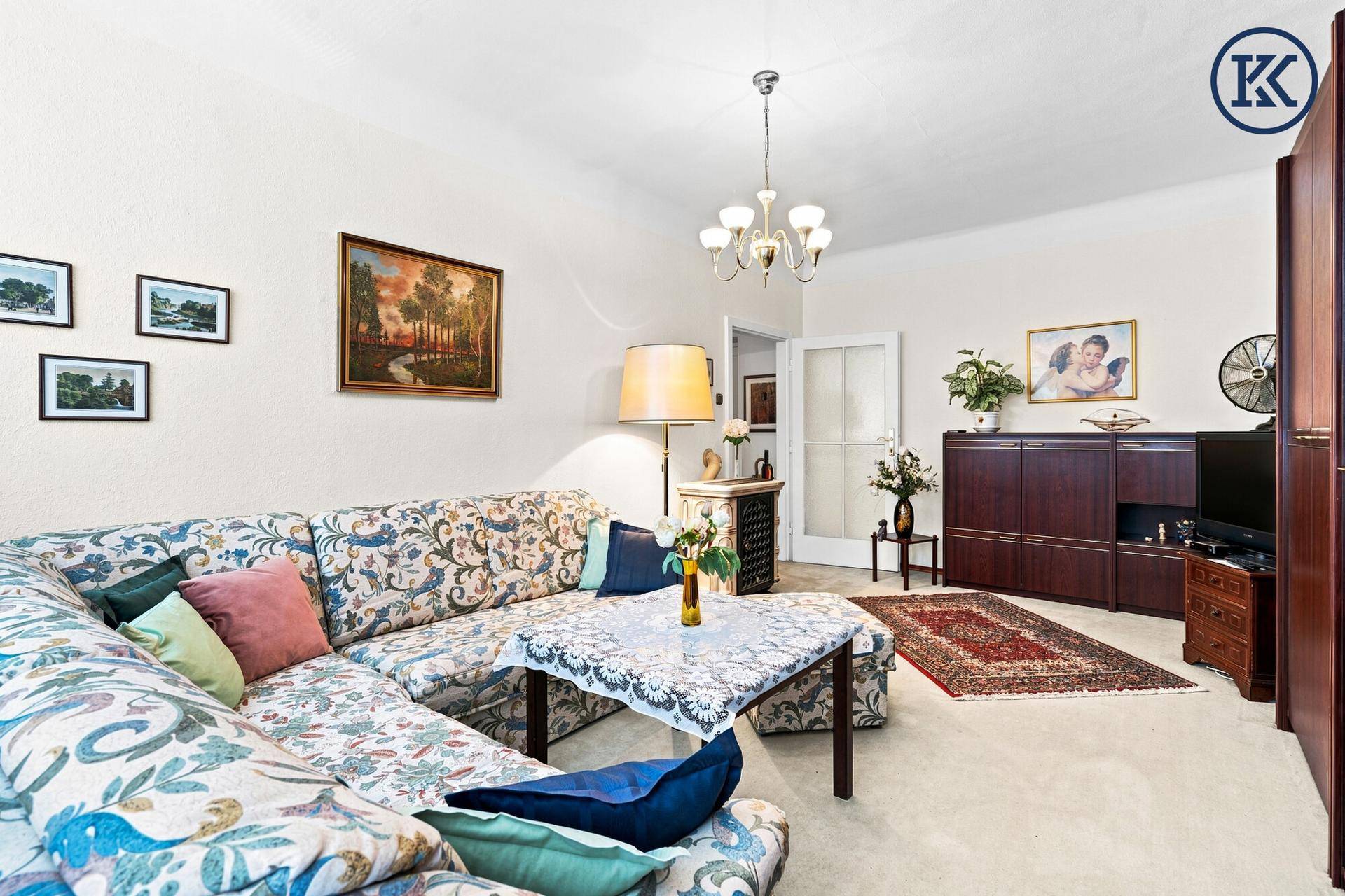 Gemütliches Wohnzimmer mit floral gemustertem Ecksofa, traditionellen Teppichen und klassischer Einrichtung.