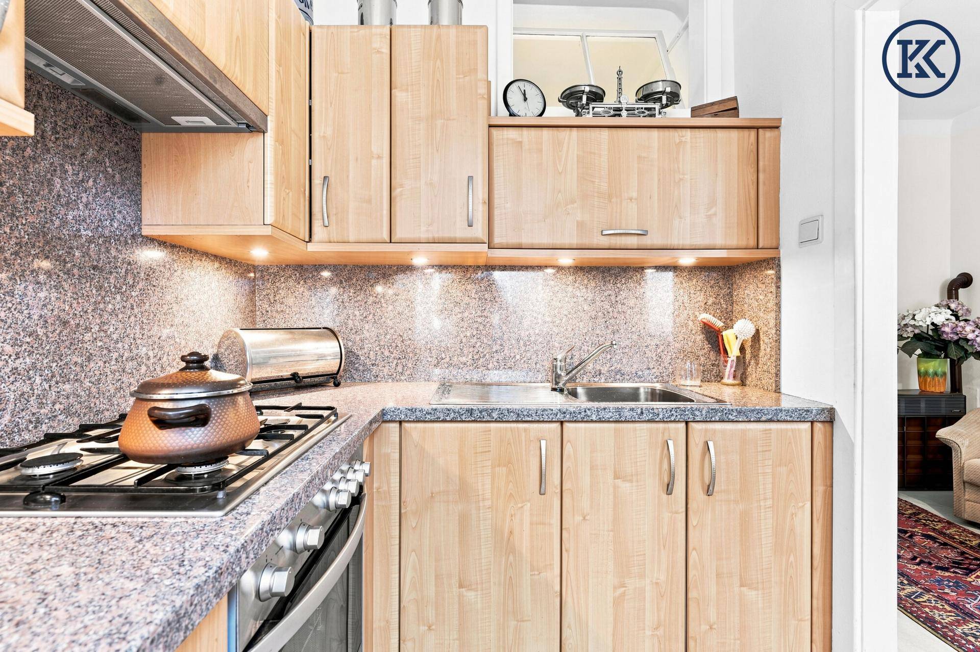 Funktionale Küche mit hellen Holzschränken, gesprenkelter Granitarbeitsplatte und Gasherd mit Backofen.