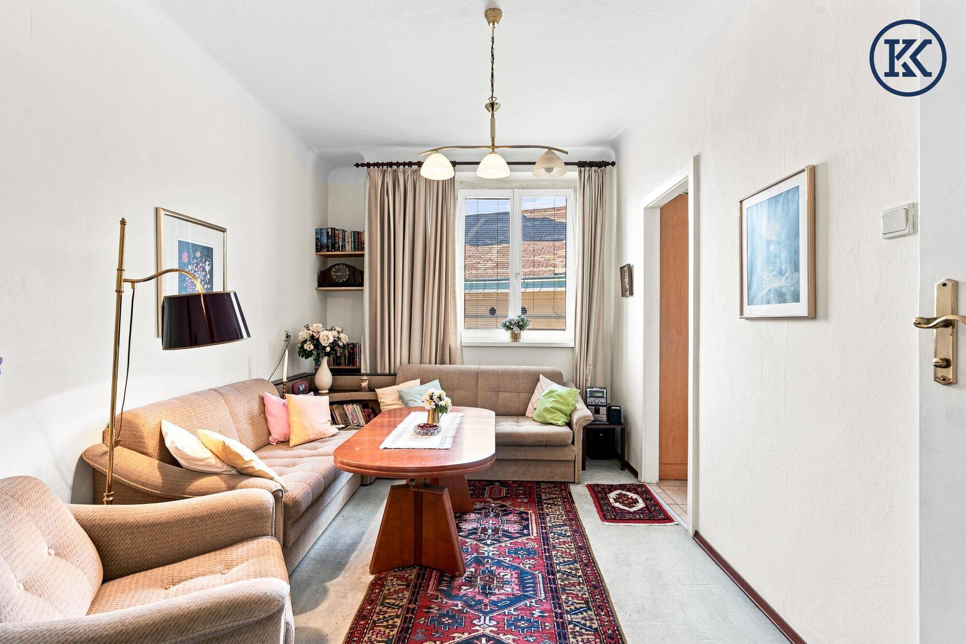 Helles Wohnzimmer mit beigem Sofa, Holztisch und einem Fenster, das viel Tageslicht hereinlässt.