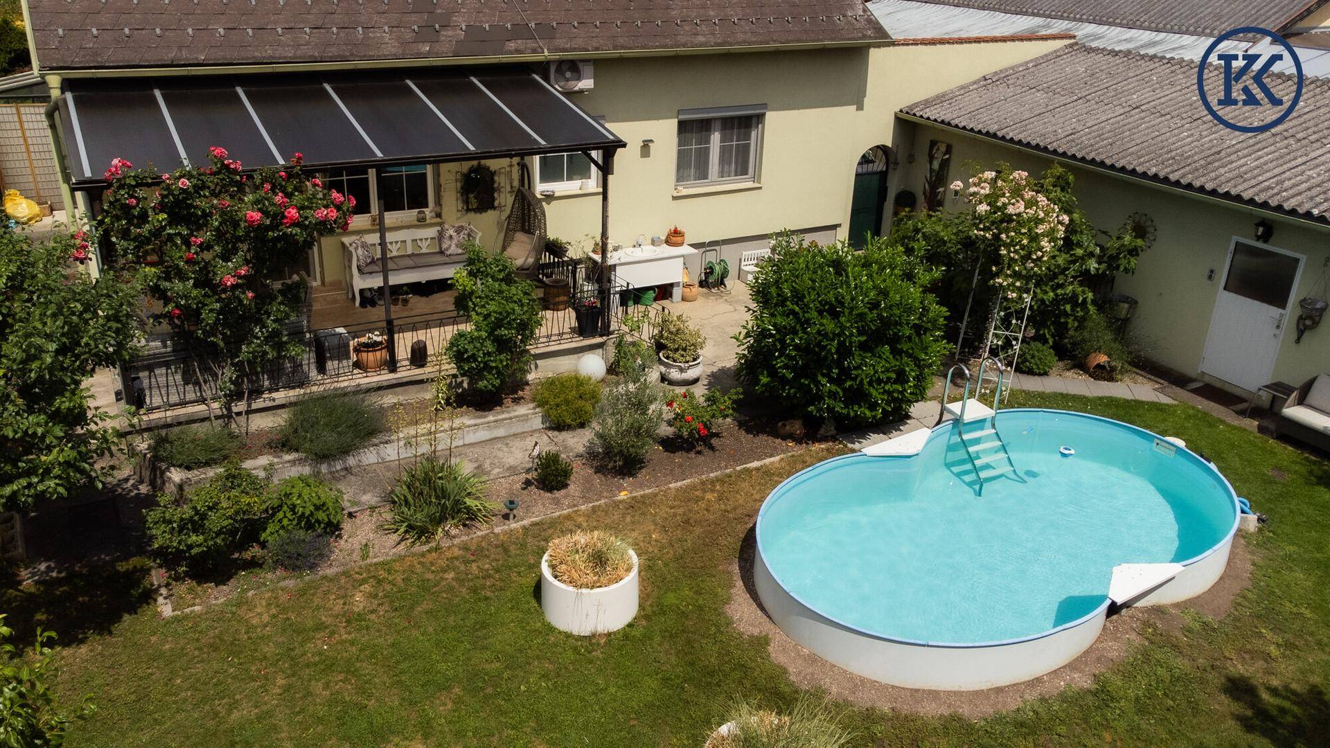 Gepflegter Garten mit ovalem Aufstellpool und überdachter Terrasse am Haus.