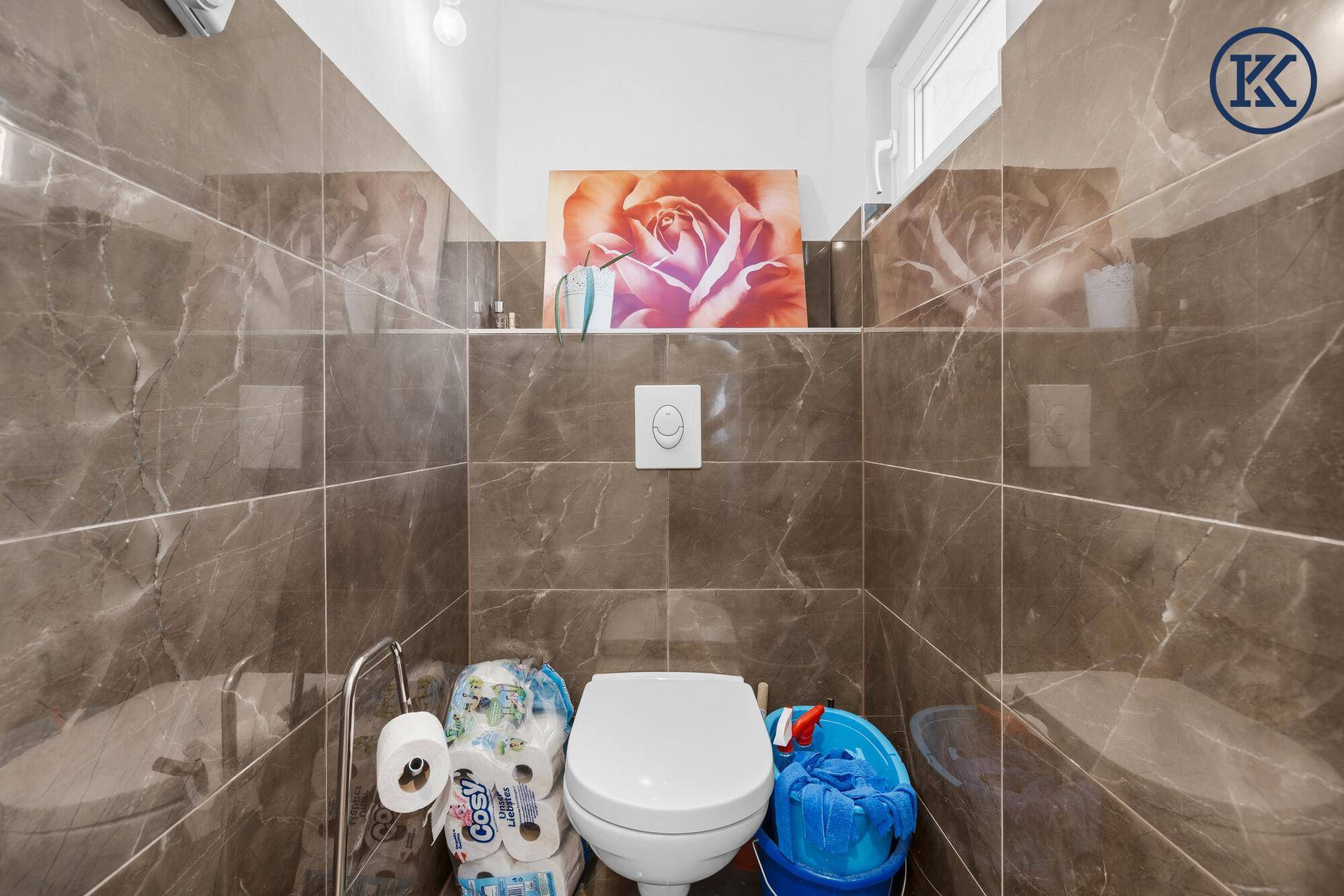 Kleines WC mit braunen Fliesen, Toilette und Fenster für Belüftung.
