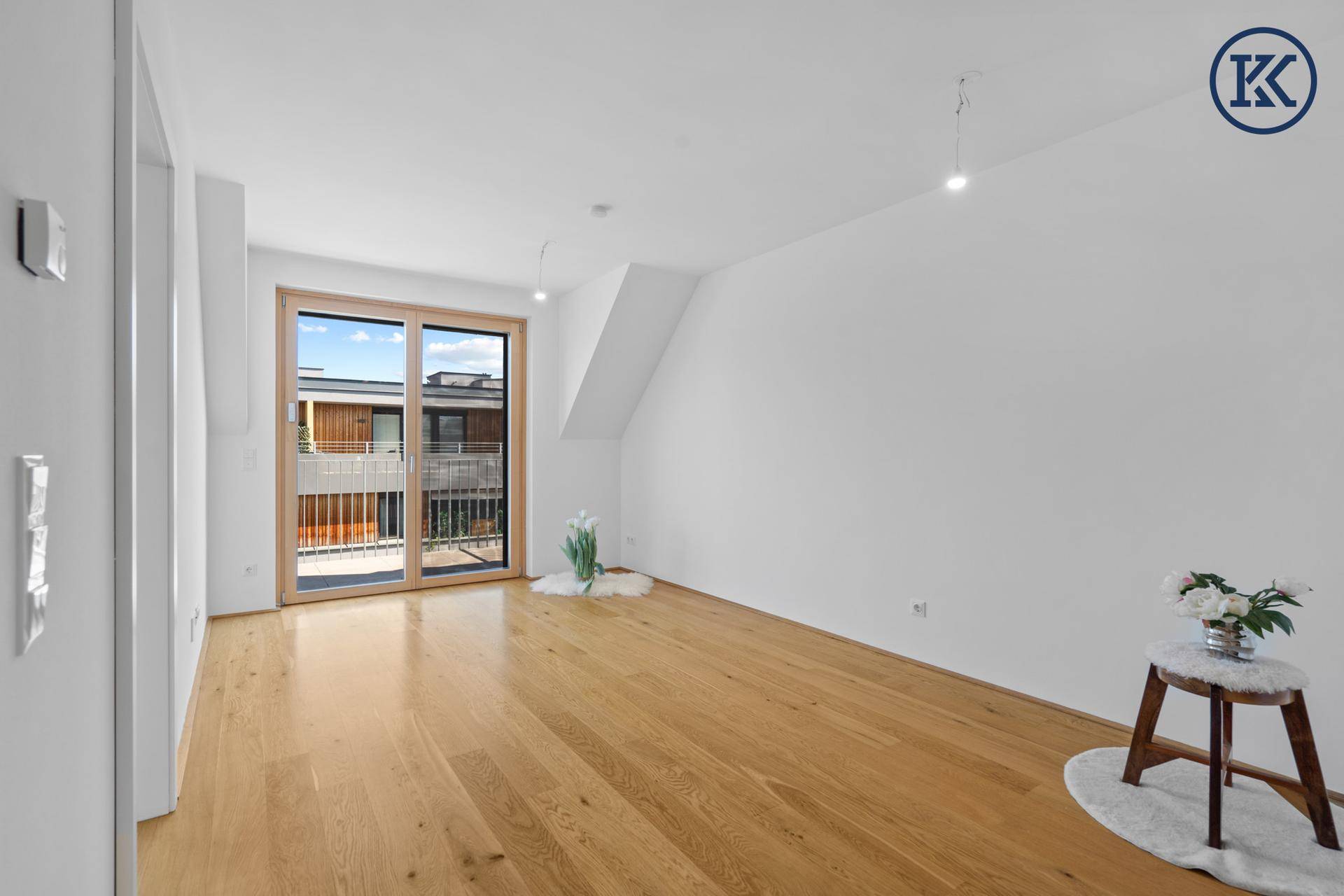 Geräumiges, leeres Wohnzimmer mit hellem Holzboden und großen Schiebetüren zum Balkon.