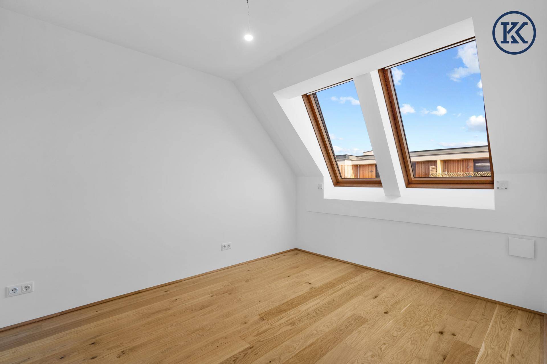 Schlafzimmer mit Holzboden und Dachfenstern, die viel natürliches Licht hereinlassen.