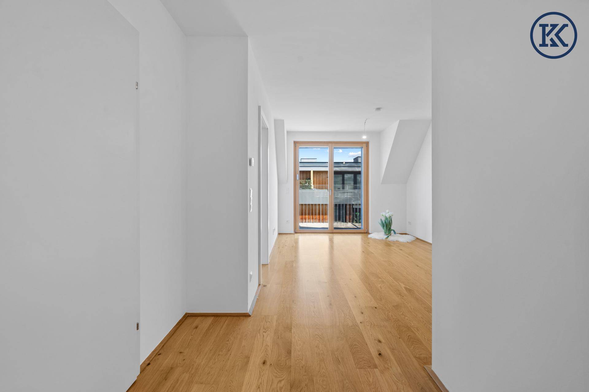 Heller Flur mit Holzboden, der in einen Wohnbereich mit Balkonzugang führt.