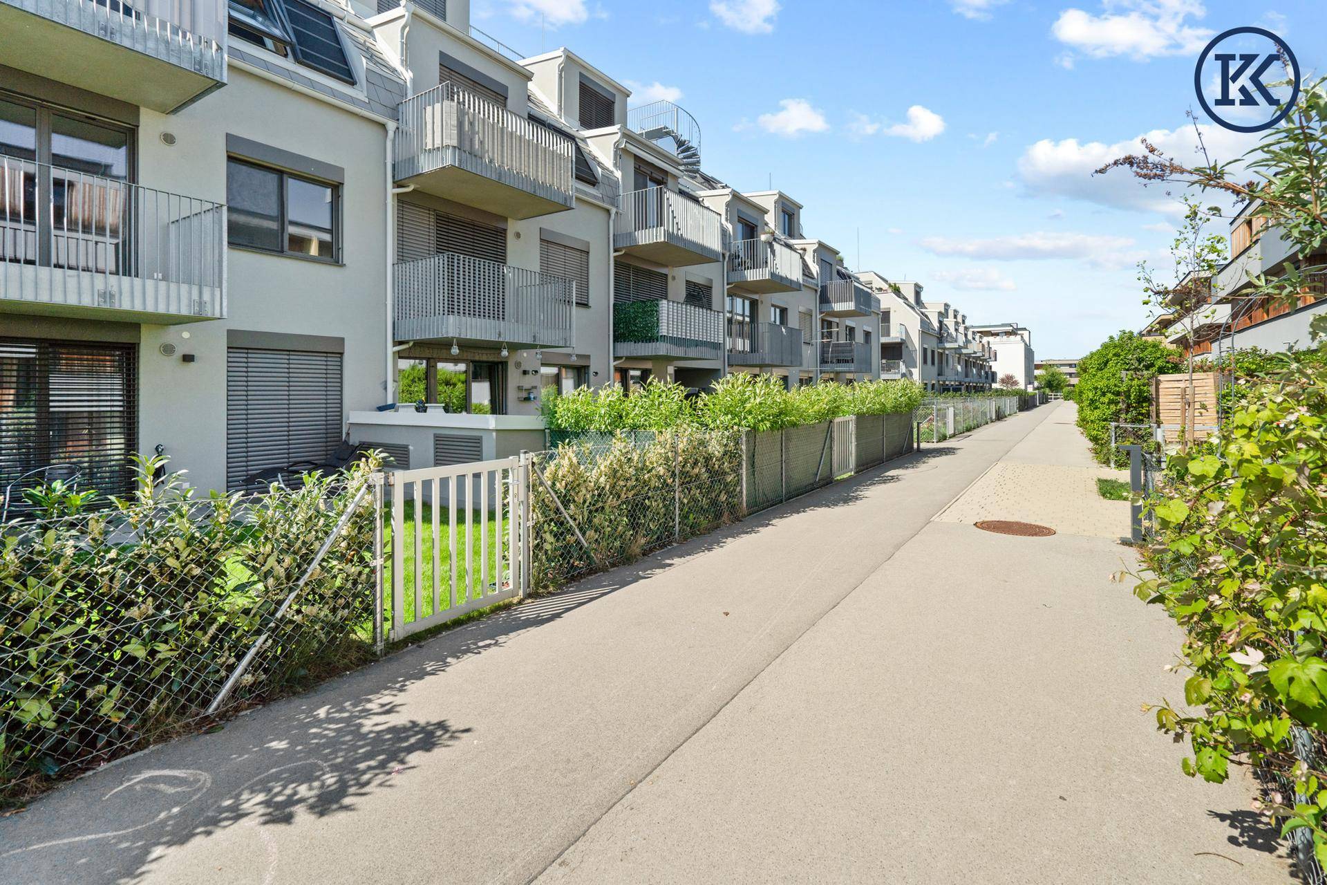 Moderne Wohngebäude mit Balkonen und begrünten Hecken entlang eines Fußwegs.