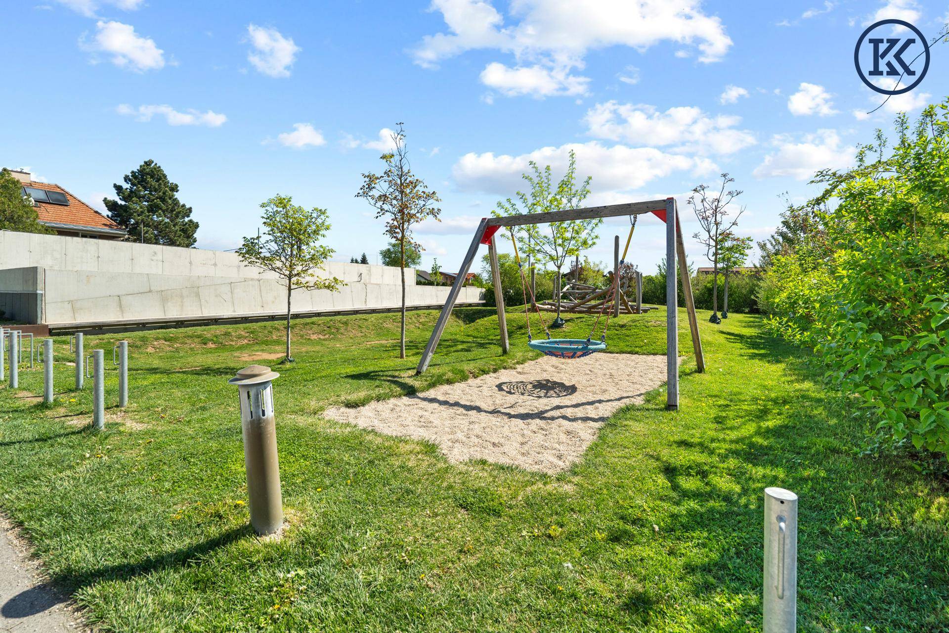 Kinderspielplatz mit Schaukeln und Sandkasten in einer grünen Parkanlage.