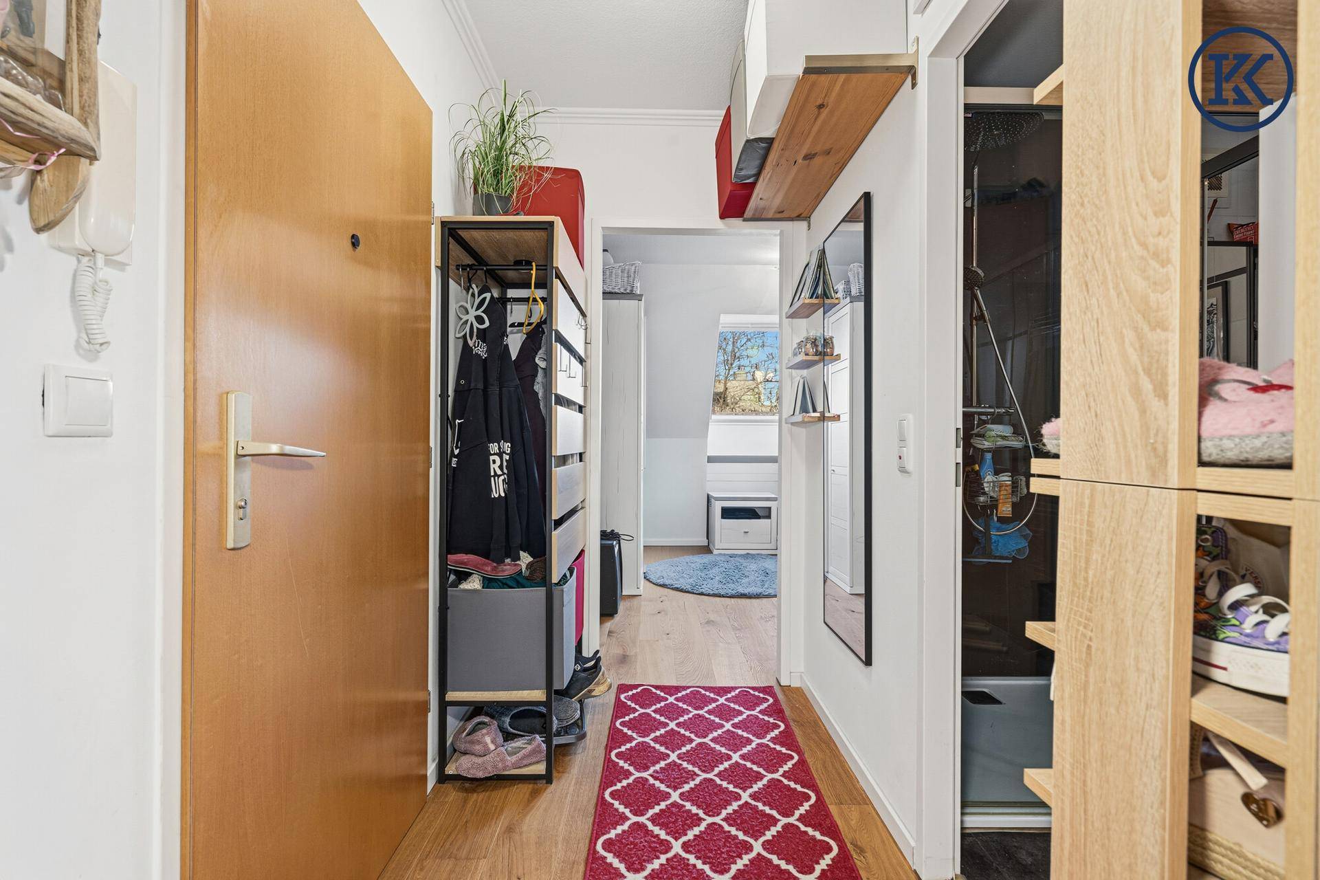 Heller Flur mit Holzfußboden, Garderobe und Spiegel, der zum Wohnbereich führt.