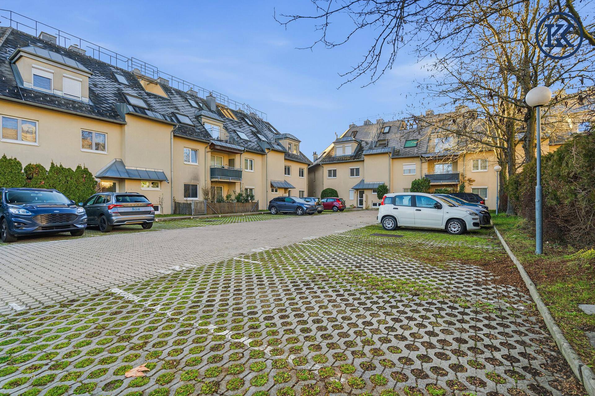 Außenansicht der Wohnanlage mit Parkplätzen und begrünten Flächen an einem sonnigen Tag.