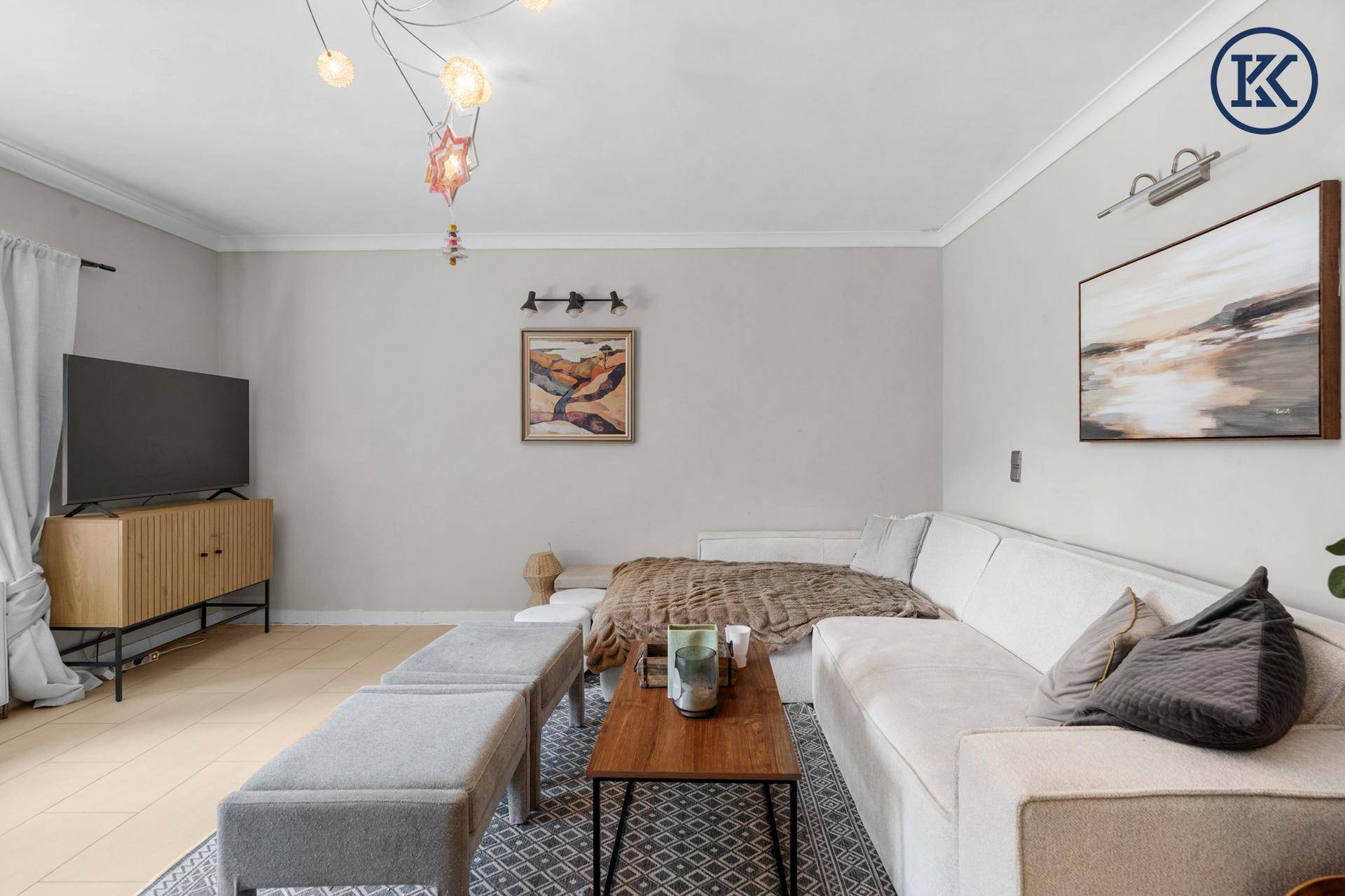 Gemütlicher Wohnbereich mit hellem Sofa, Couchtisch und Fernseher vor einem großen Fenster.