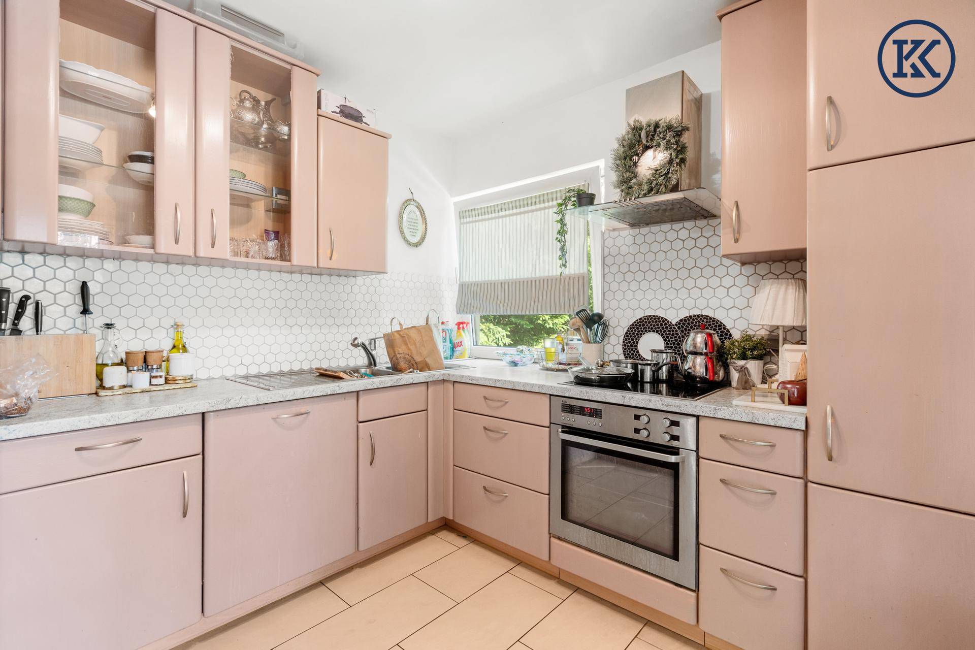 Küche mit rosa Schränken, weißen sechseckigen Fliesen und integriertem Backofen unter dem Fenster.
