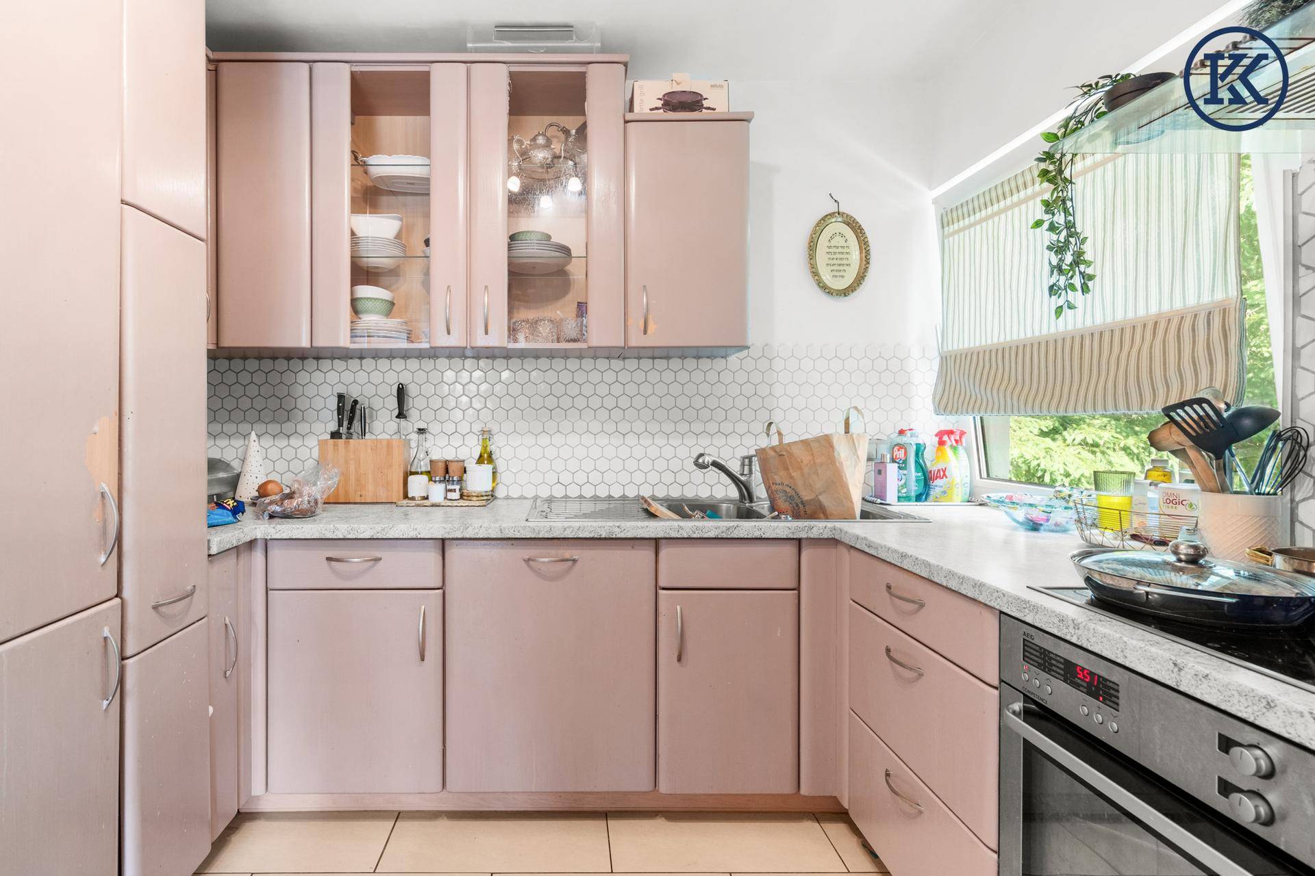 Funktionale Küche mit rosa Fronten, hellen Arbeitsplatten und Fenster mit Blick ins Grüne.