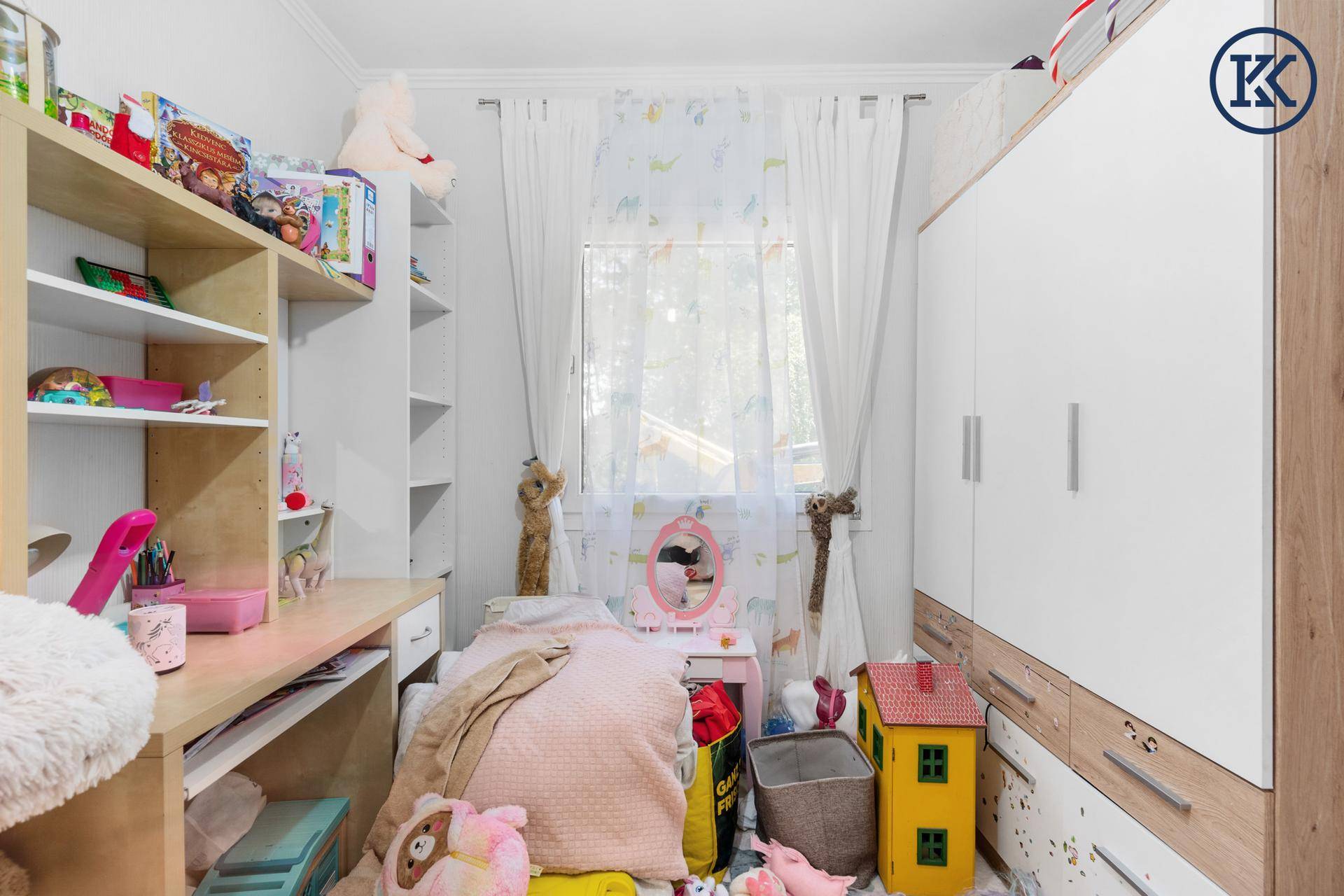 Helles Kinderzimmer mit Schreibtisch, Regalen und Fenster mit Vorhängen.