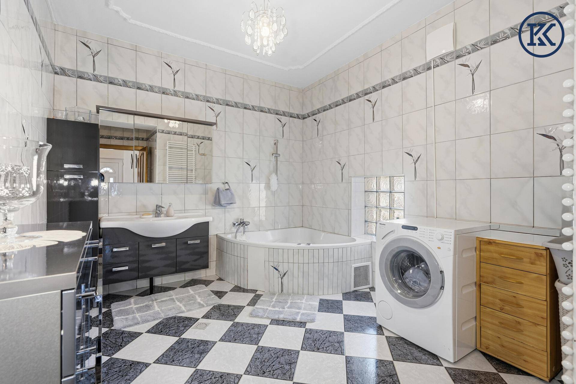 Großes Badezimmer mit Eckbadewanne, Dusche, Waschmaschine und schwarz-weißem Fliesenboden.