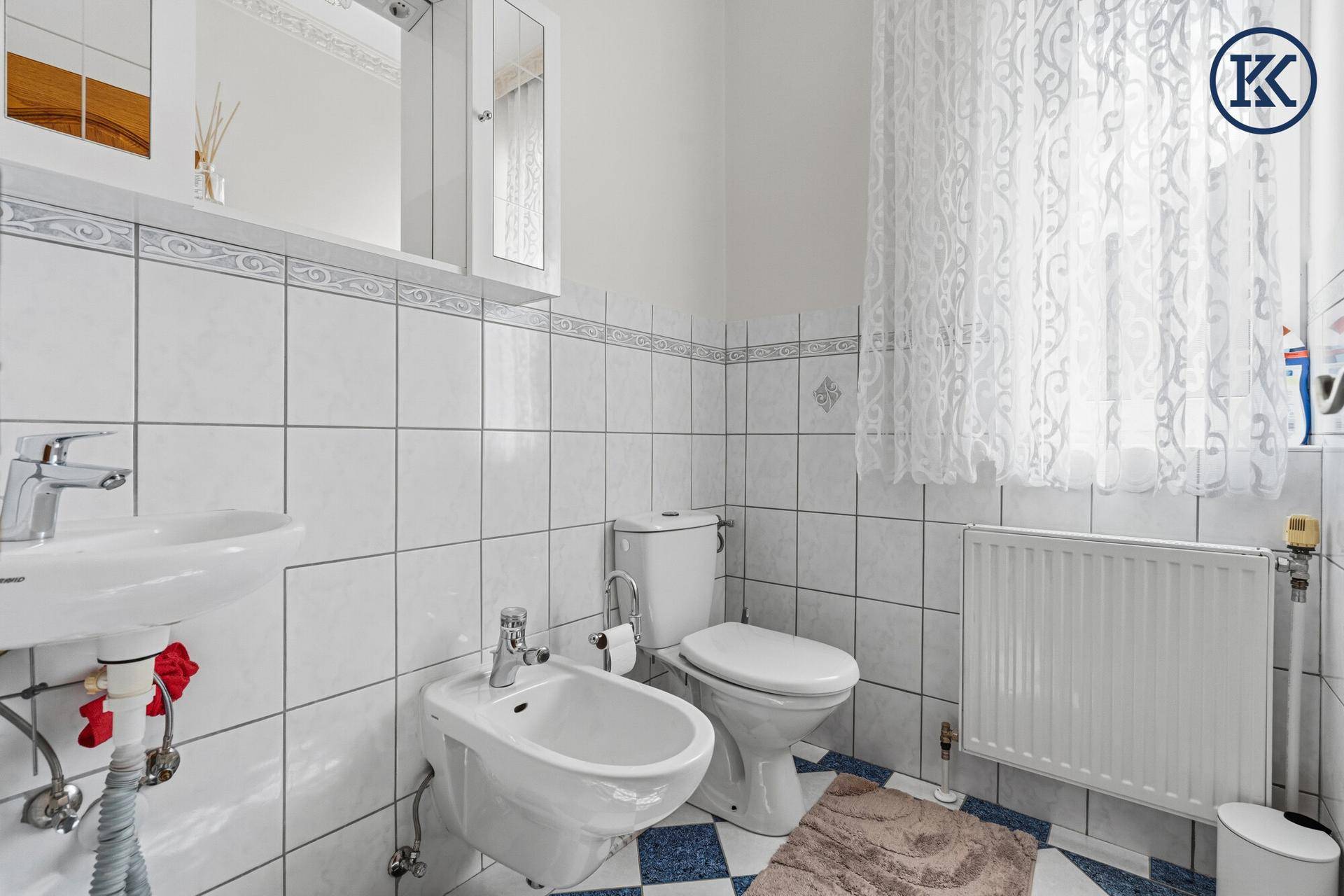 Kleines Badezimmer mit WC, Bidet, Waschbecken und weiß-blauen Fliesen.