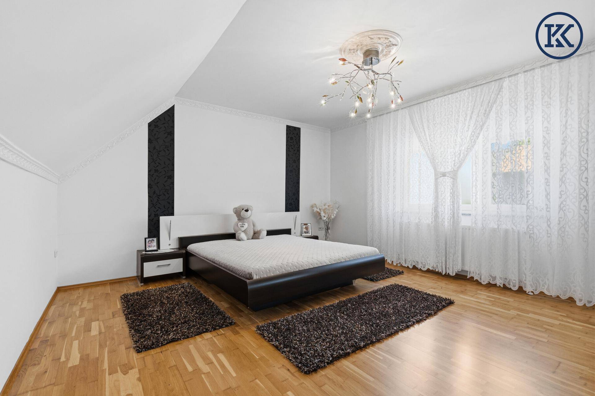 Helles Schlafzimmer mit Parkettboden, Doppelbett und weißen Vorhängen.