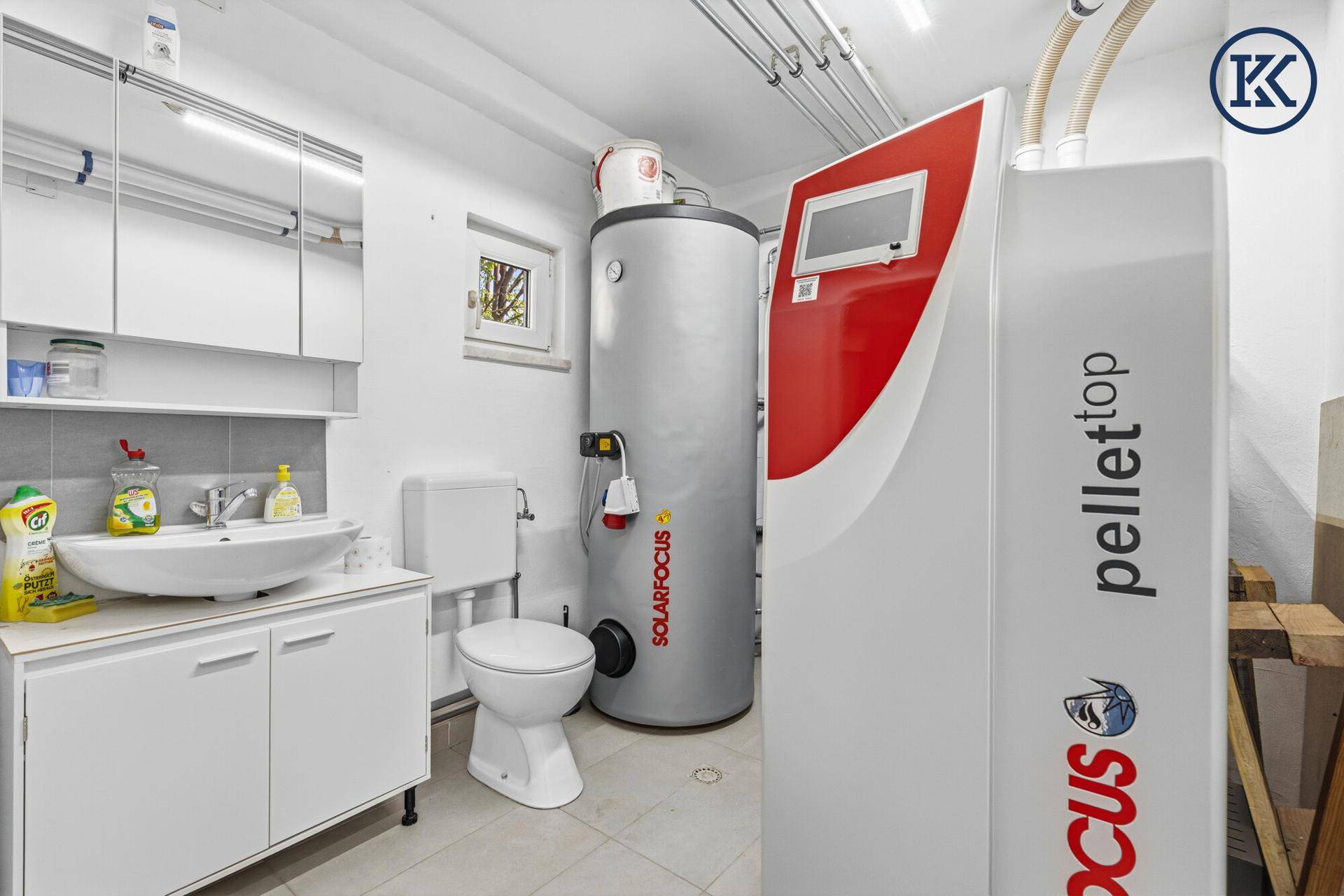 Hauswirtschaftsraum mit Pelletheizung, Warmwasserspeicher, WC und Waschbecken.