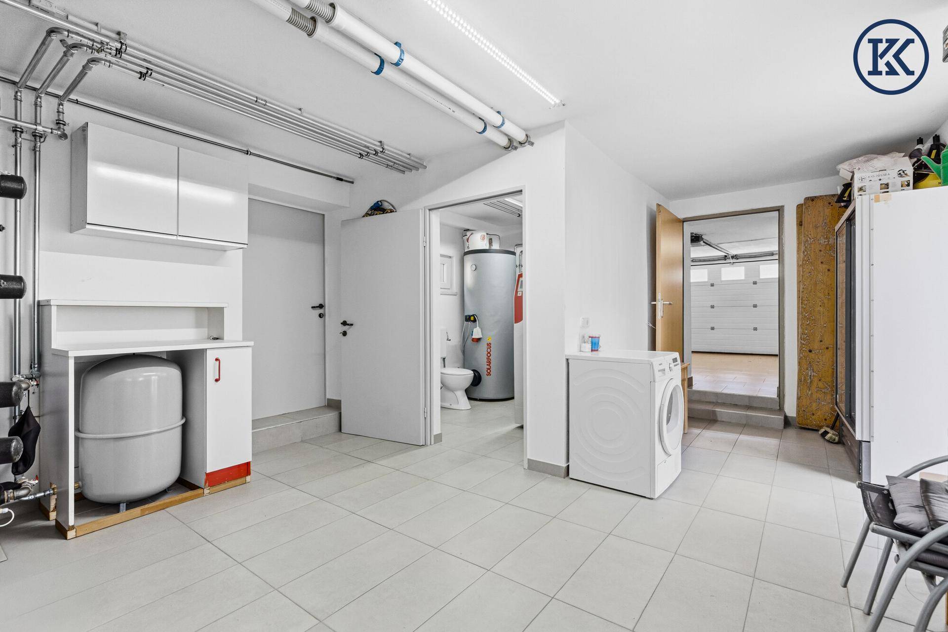 Heller Hauswirtschaftsraum mit Waschmaschine, Fliesenboden und Zugang zur Garage.