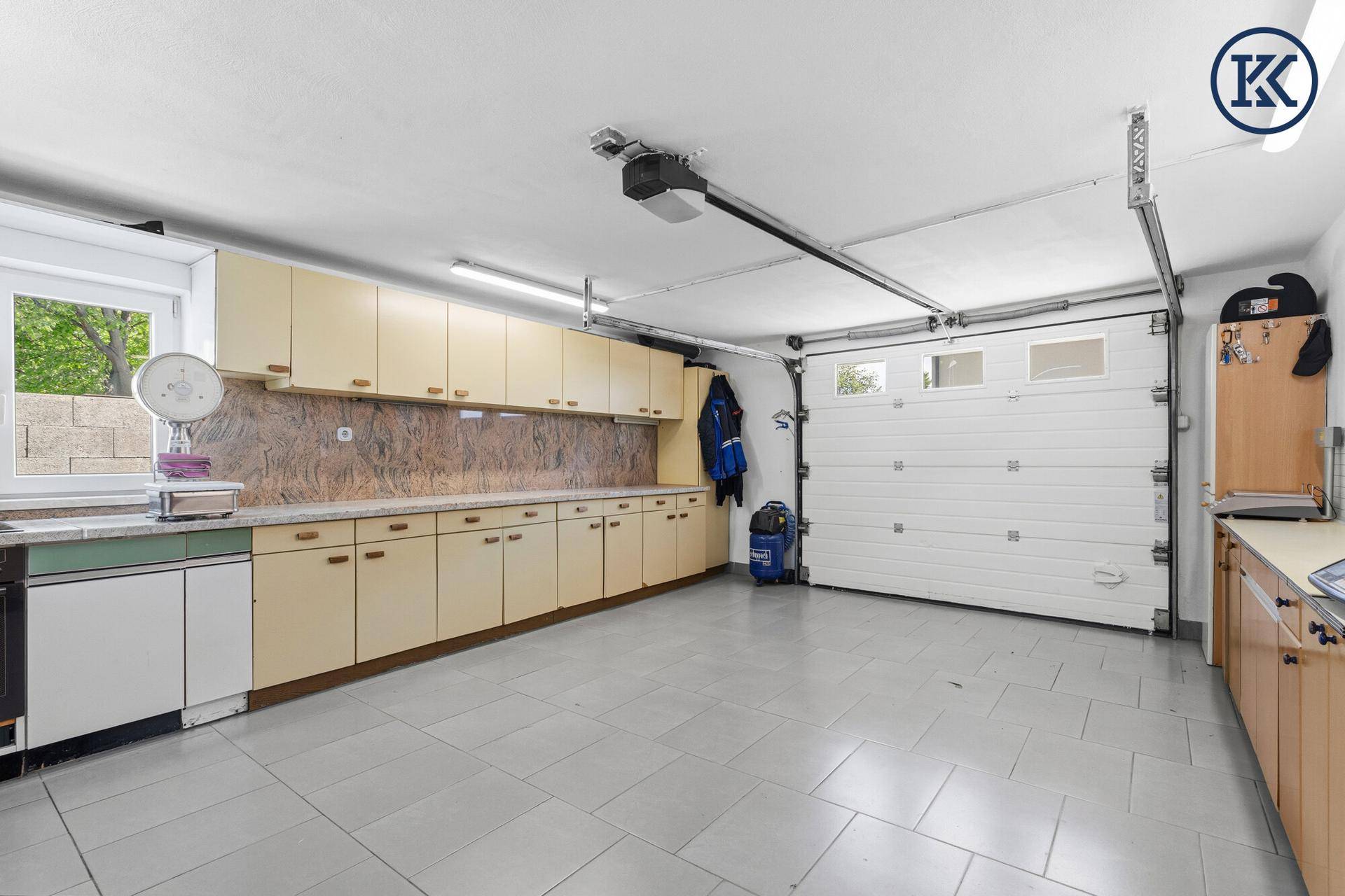 Geräumige Garage mit vielen Einbauschränken, Fliesenboden und automatischem Garagentor.