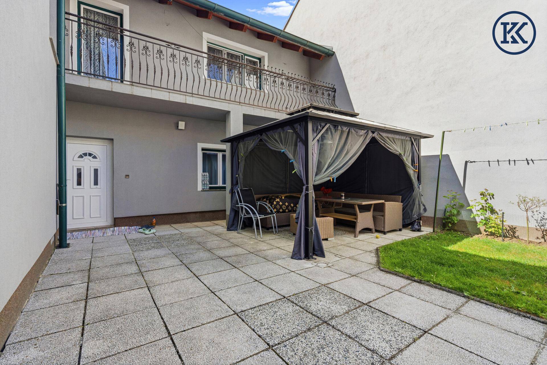 Gemütlicher überdachter Sitzbereich im Garten mit Gartenmöbeln und Blick auf den Balkon.