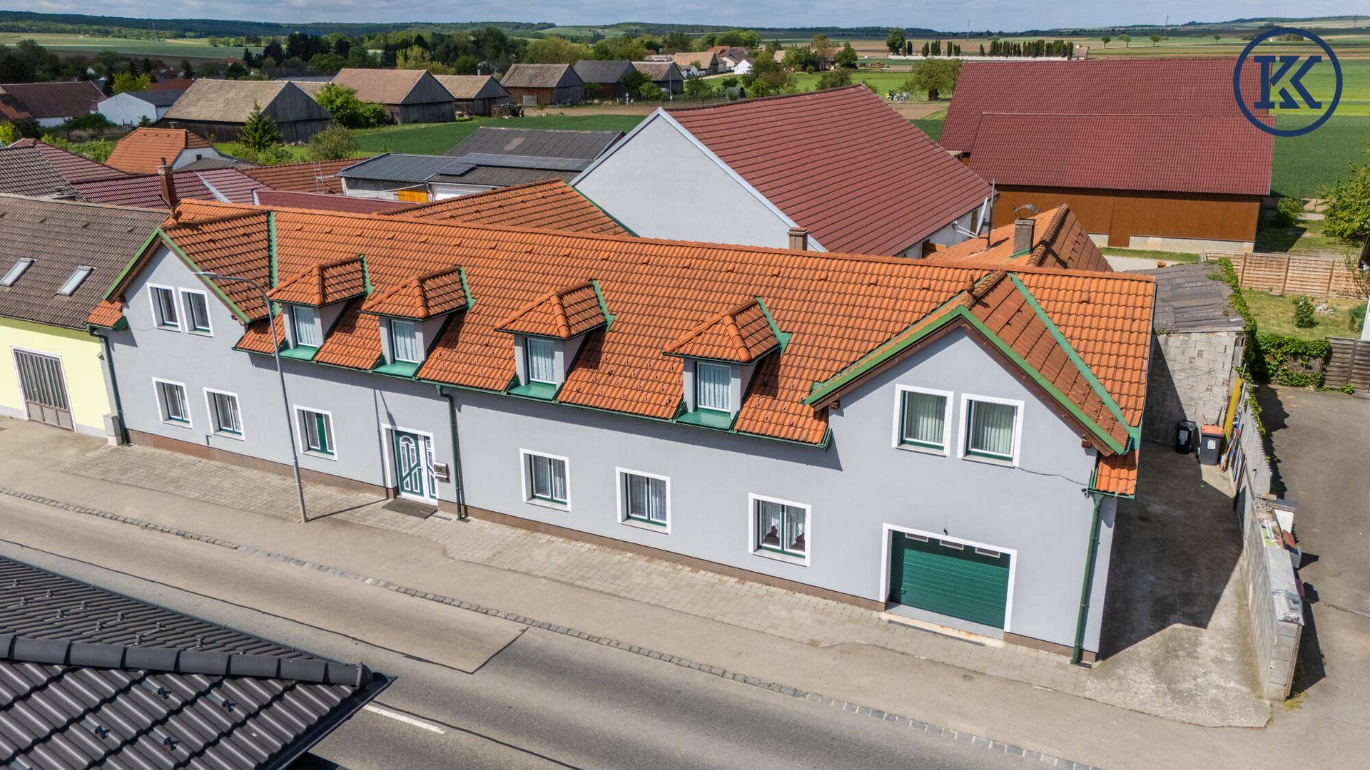 Vogelperspektive des Wohnhauses mit mehreren Dachgauben und angrenzenden Feldern.