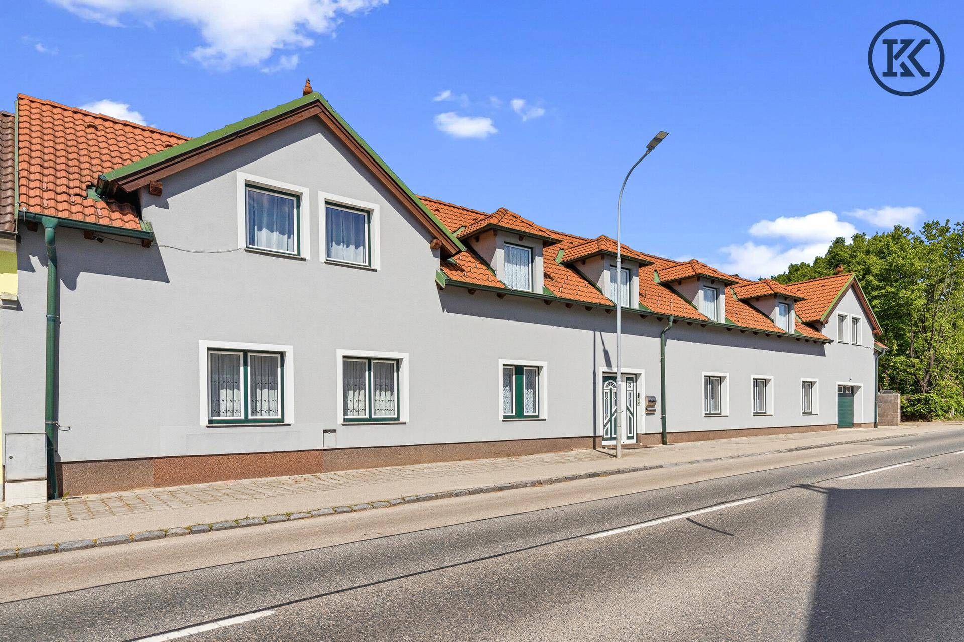 Langes Wohngebäude mit mehreren Gauben, Ziegeldach und direkter Straßenanbindung.