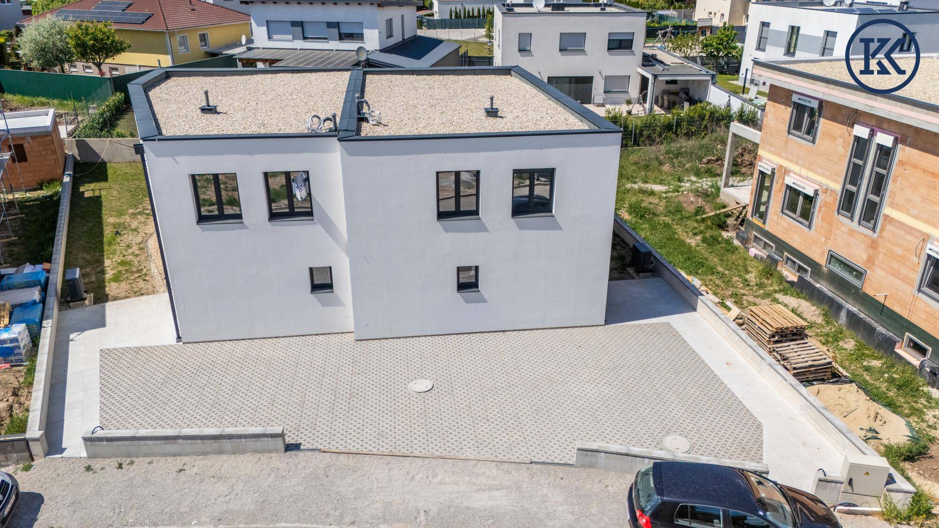 Schräge Luftaufnahme der modernen Doppelhaushälfte mit großem Vorplatz und Flachdach.