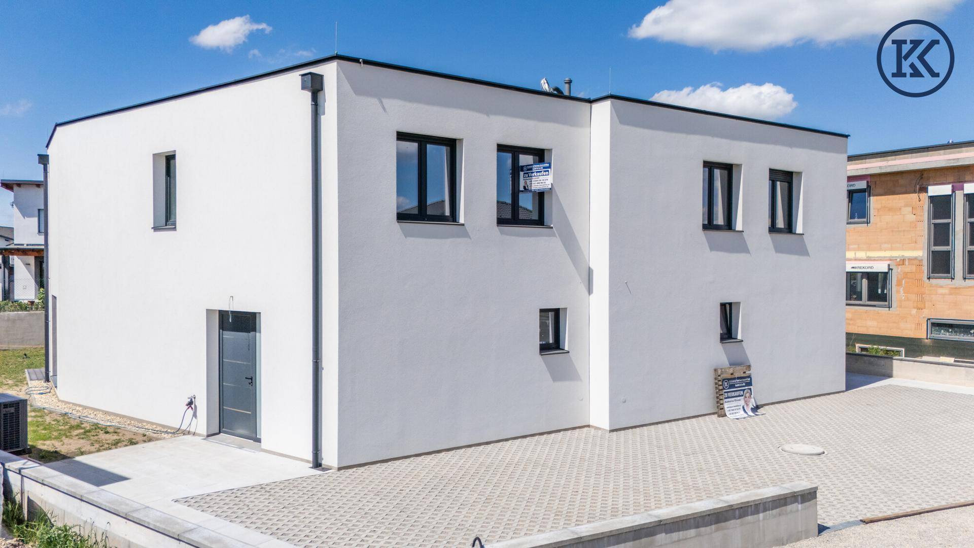 Moderne Doppelhaushälfte von der Seite mit Eingangsbereich und großem Parkplatz im Freien.