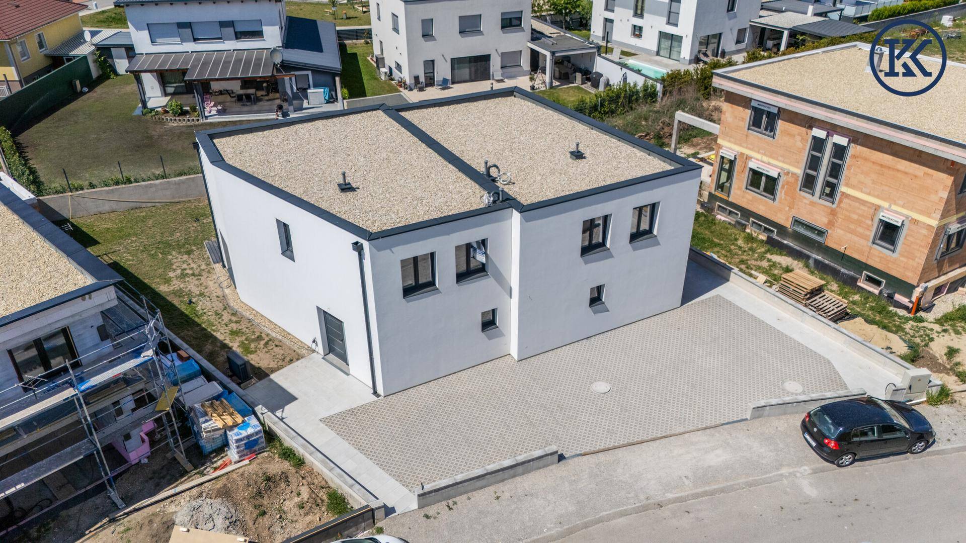 Vogelperspektive der Doppelhaushälfte mit gepflastertem Parkbereich und umliegenden Neubauten.