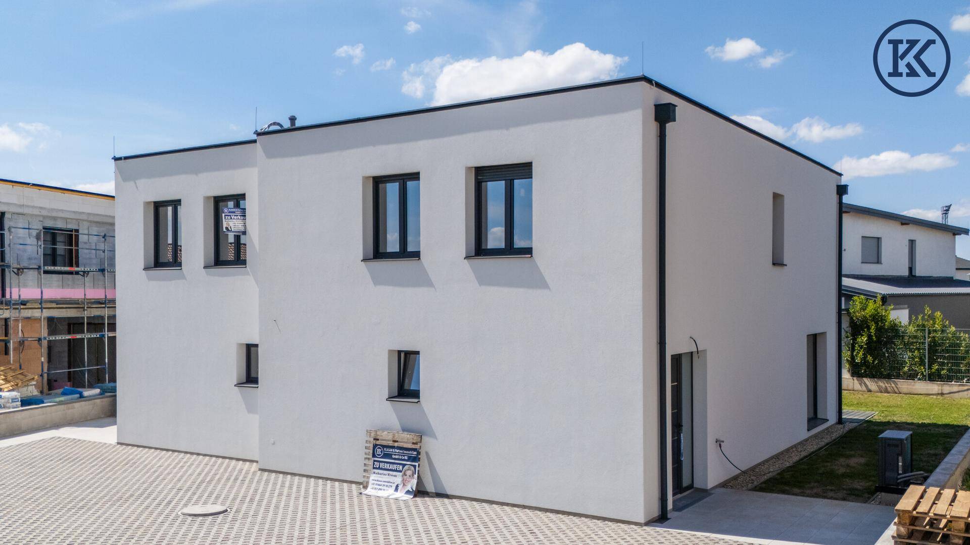 Seitenansicht der Doppelhaushälfte mit weißer Fassade, schwarzen Fenstern und gepflastertem Vorplatz.